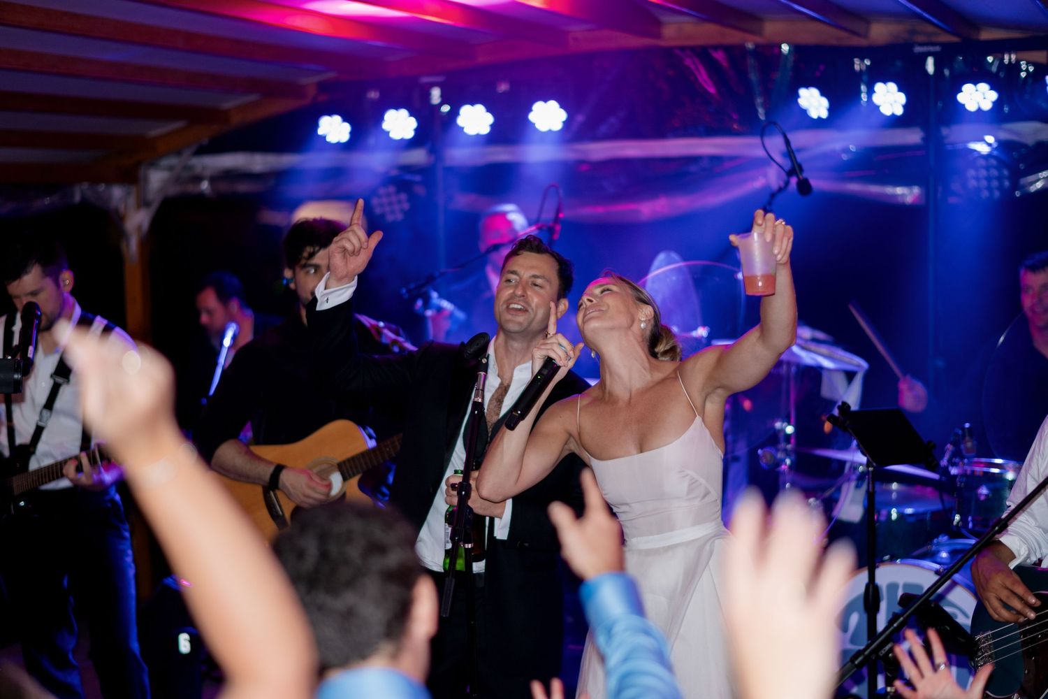 Bride and groom singing on stage with live band at wedding reception party with blue lights.