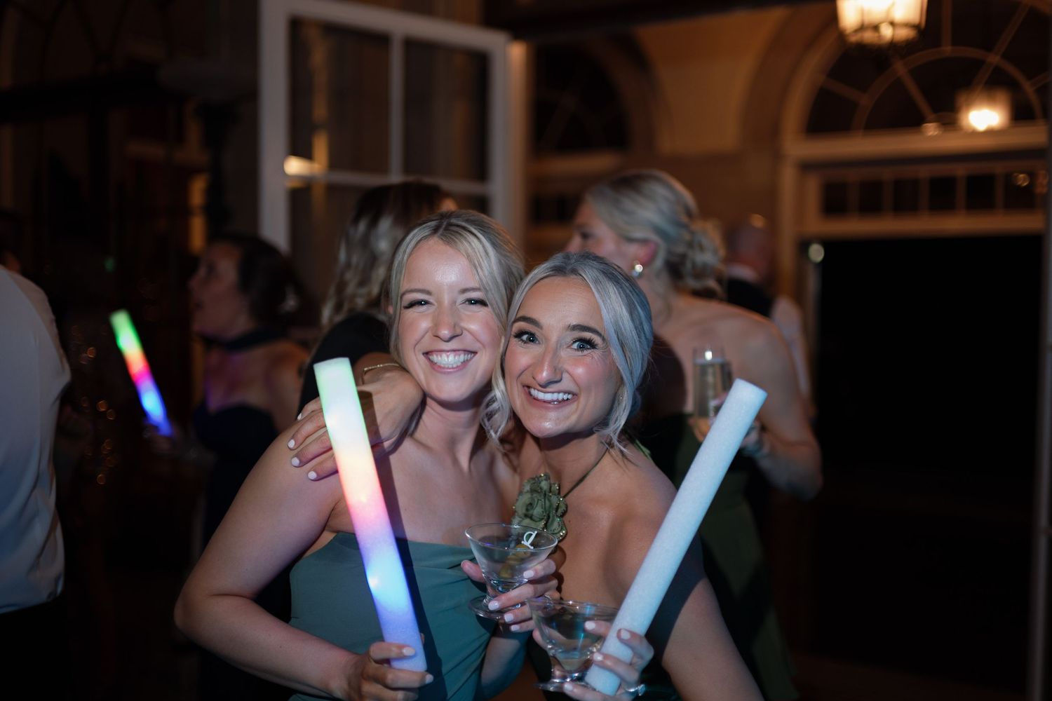 Party guests pose with colorful LED light sticks at a nighttime celebration event.