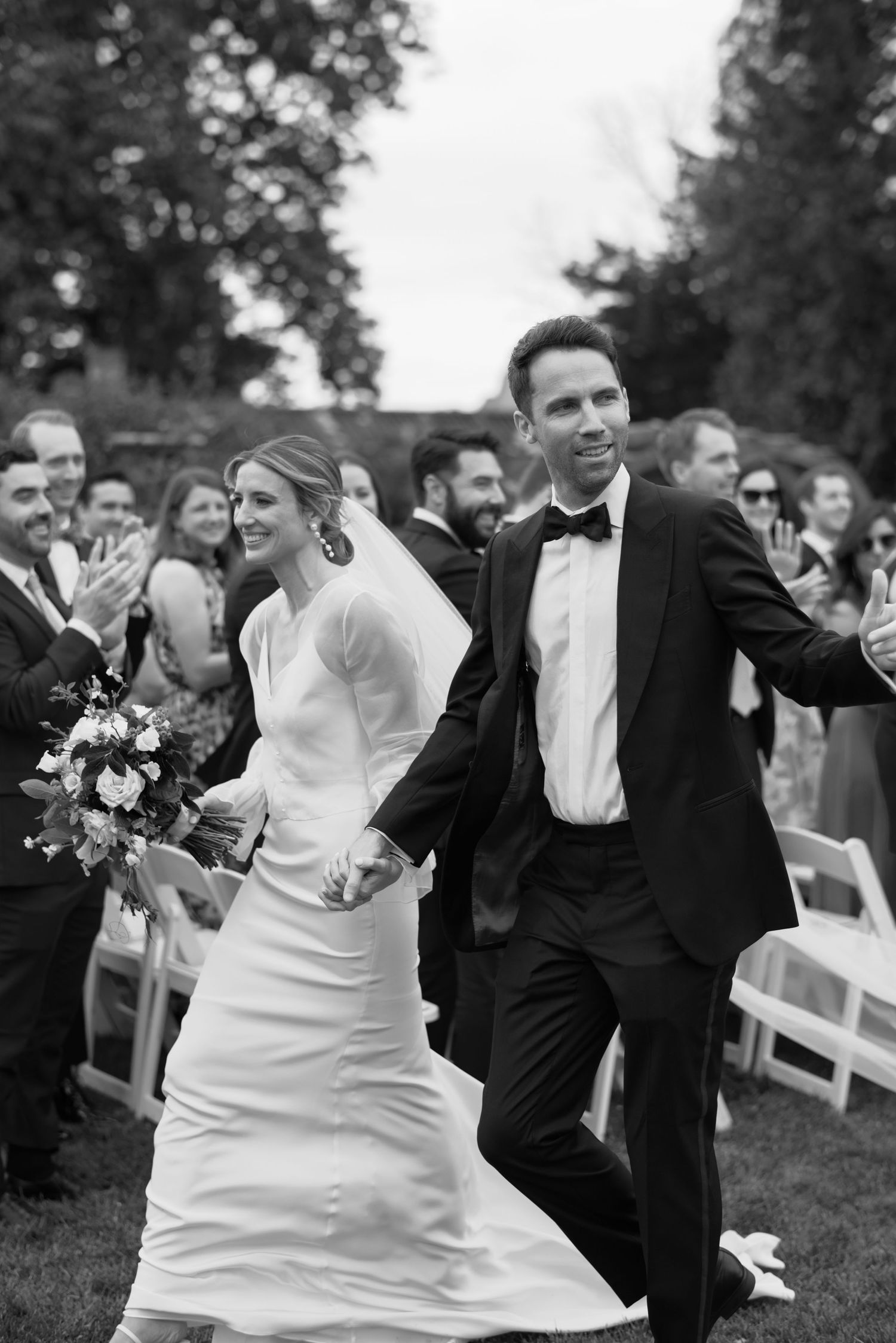A joyful couple celebrates during their wedding recessional with guests cheering in the background.