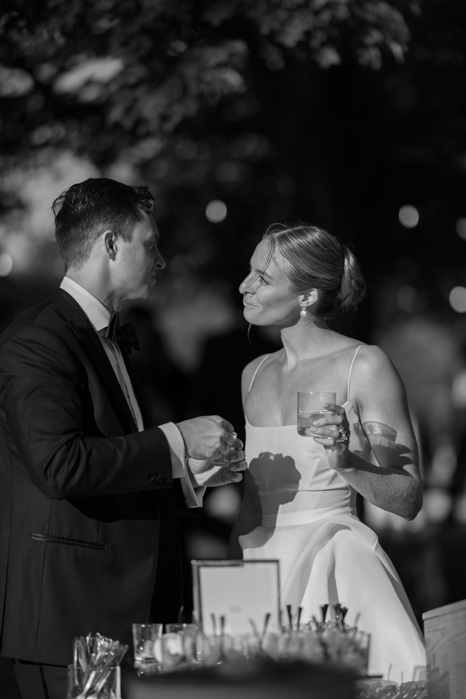 Black and white photo of a bride and groom sharing a champagne toast at their outdoor wedding reception.