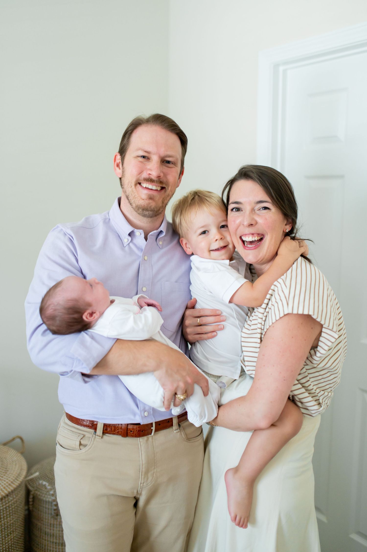 A family shares joyful moments together in a bright white room wearing casual attire.