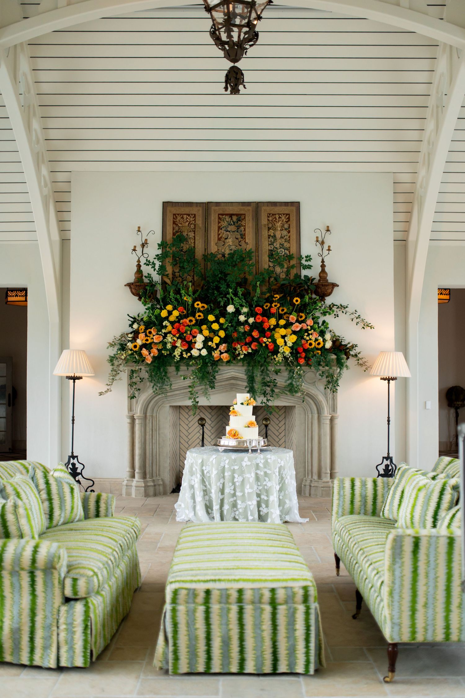 Reception area with green striped chaise lounges and floral arrangements under white beamed ceiling.