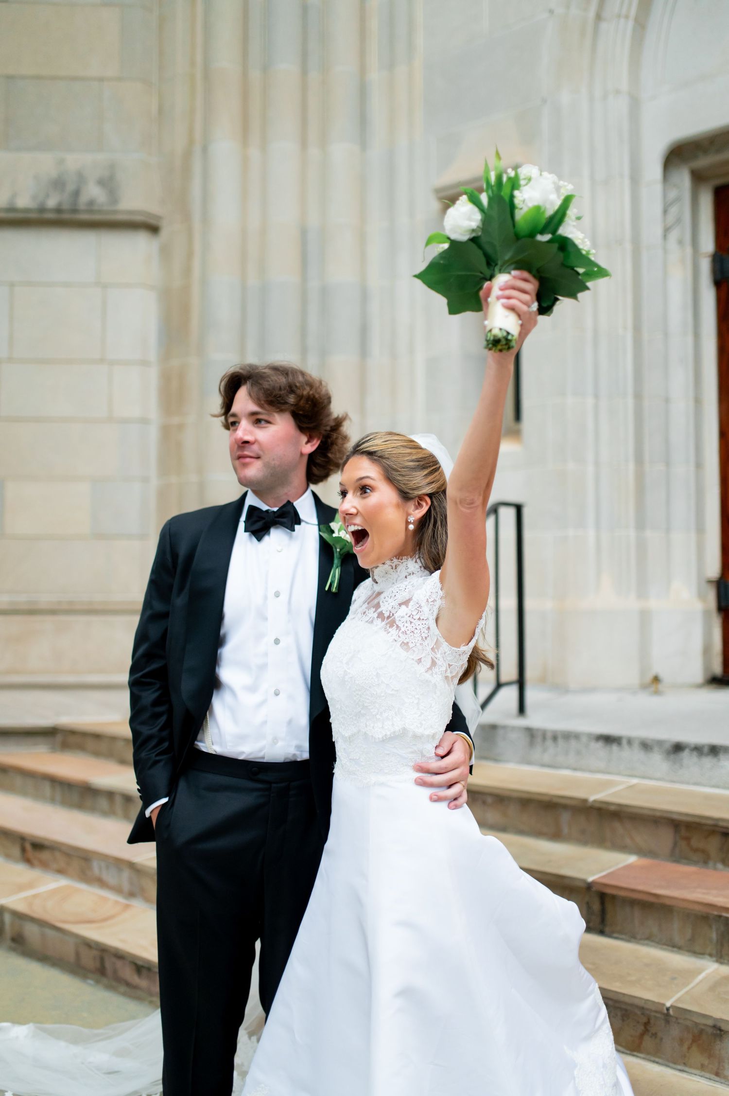 Joyful wedding celebration on cathedral steps with bride in white lace gown.