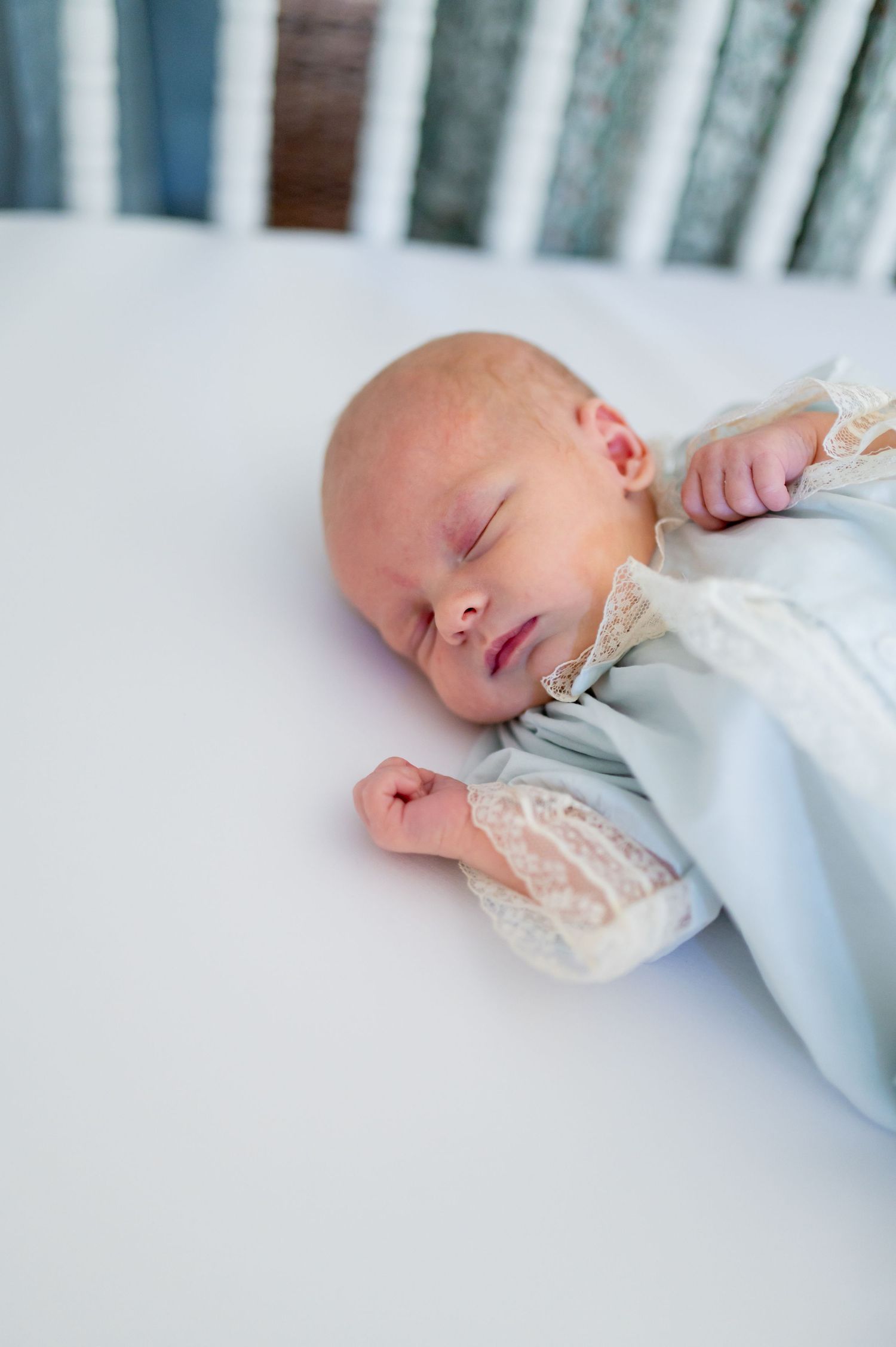 A sleeping newborn baby wearing white lace clothing rests peacefully in soft bedding.