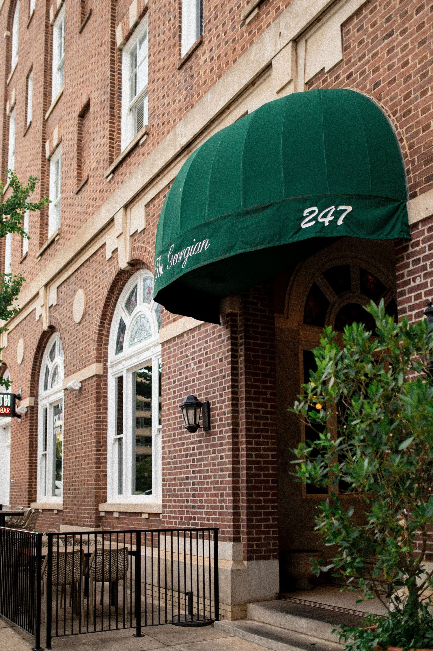 Green awning entrance of The Georgian at 247, a classic brick building with arched windows and iron railings.