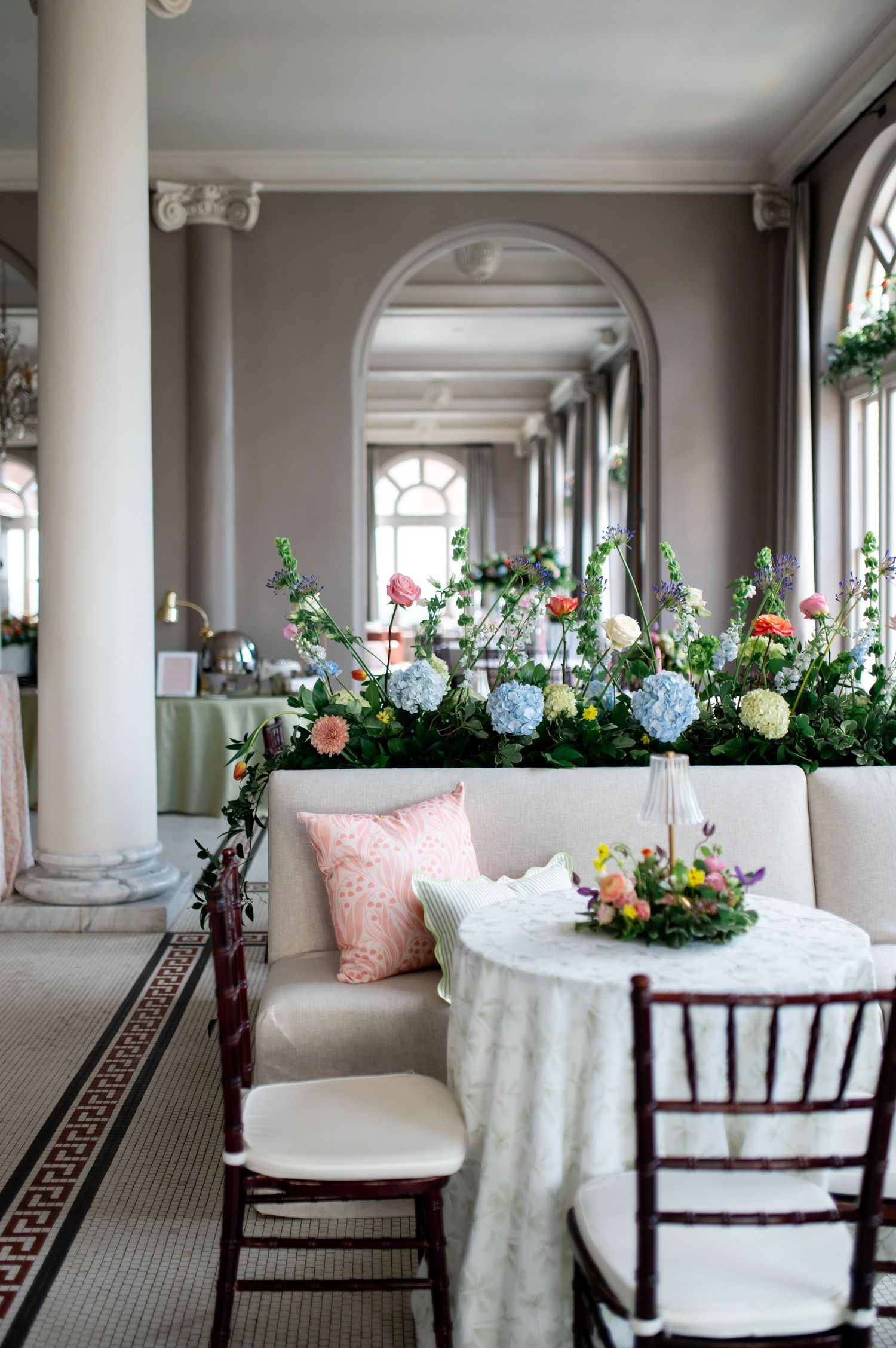 Wedding reception venue with lush floral garden display, chiavari chairs, and arched columns.