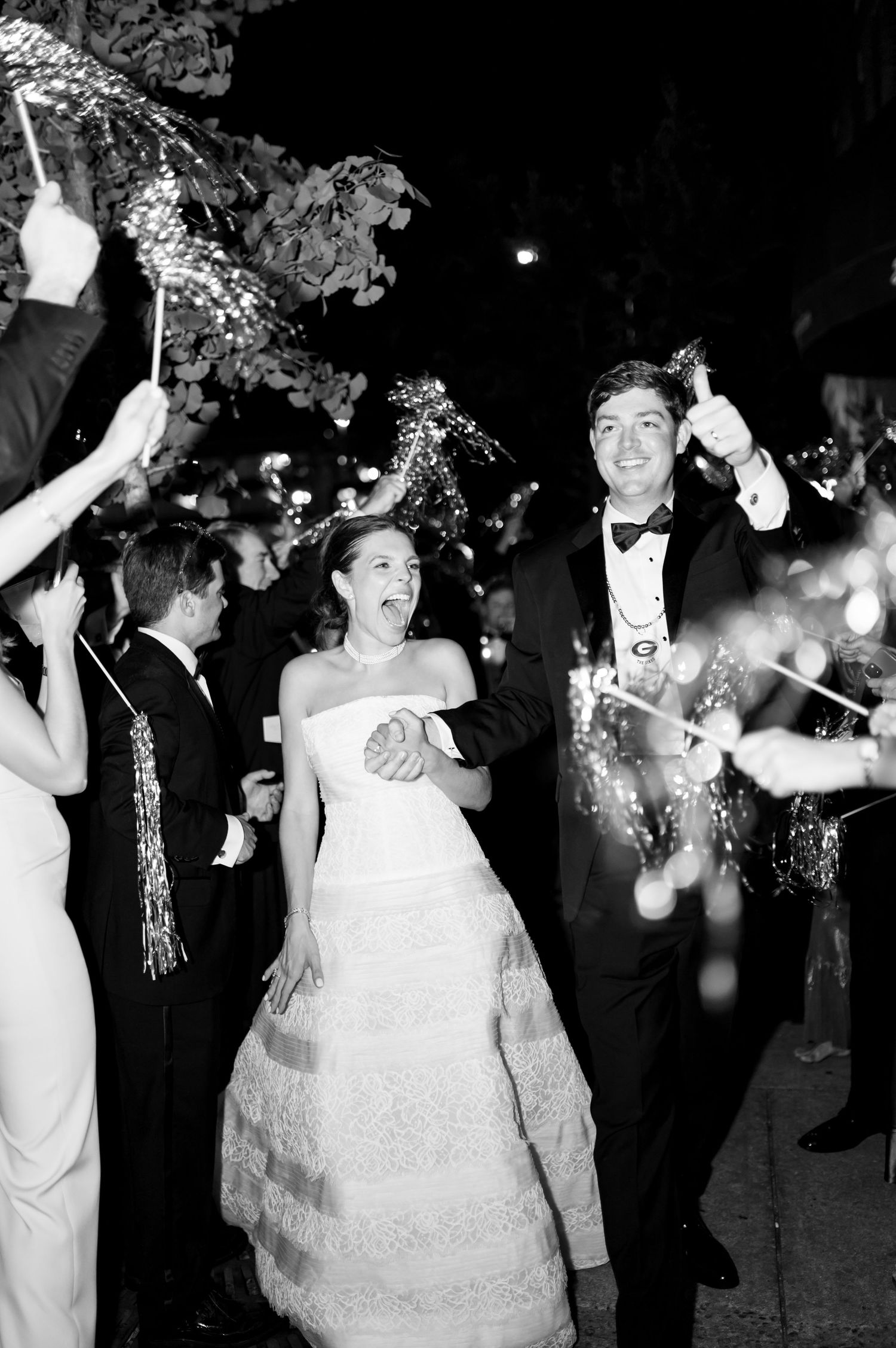 Bride and groom exiting wedding reception through sparkler and tinsel send-off in black and white.