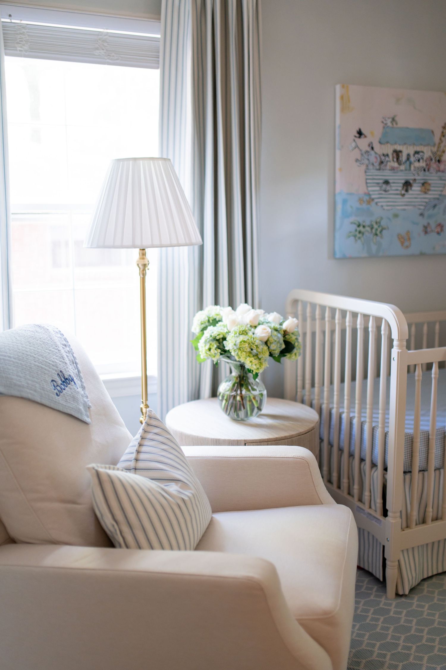 A serene nursery corner featuring a white armchair, floor lamp, and fresh hydrangeas next to a white crib.