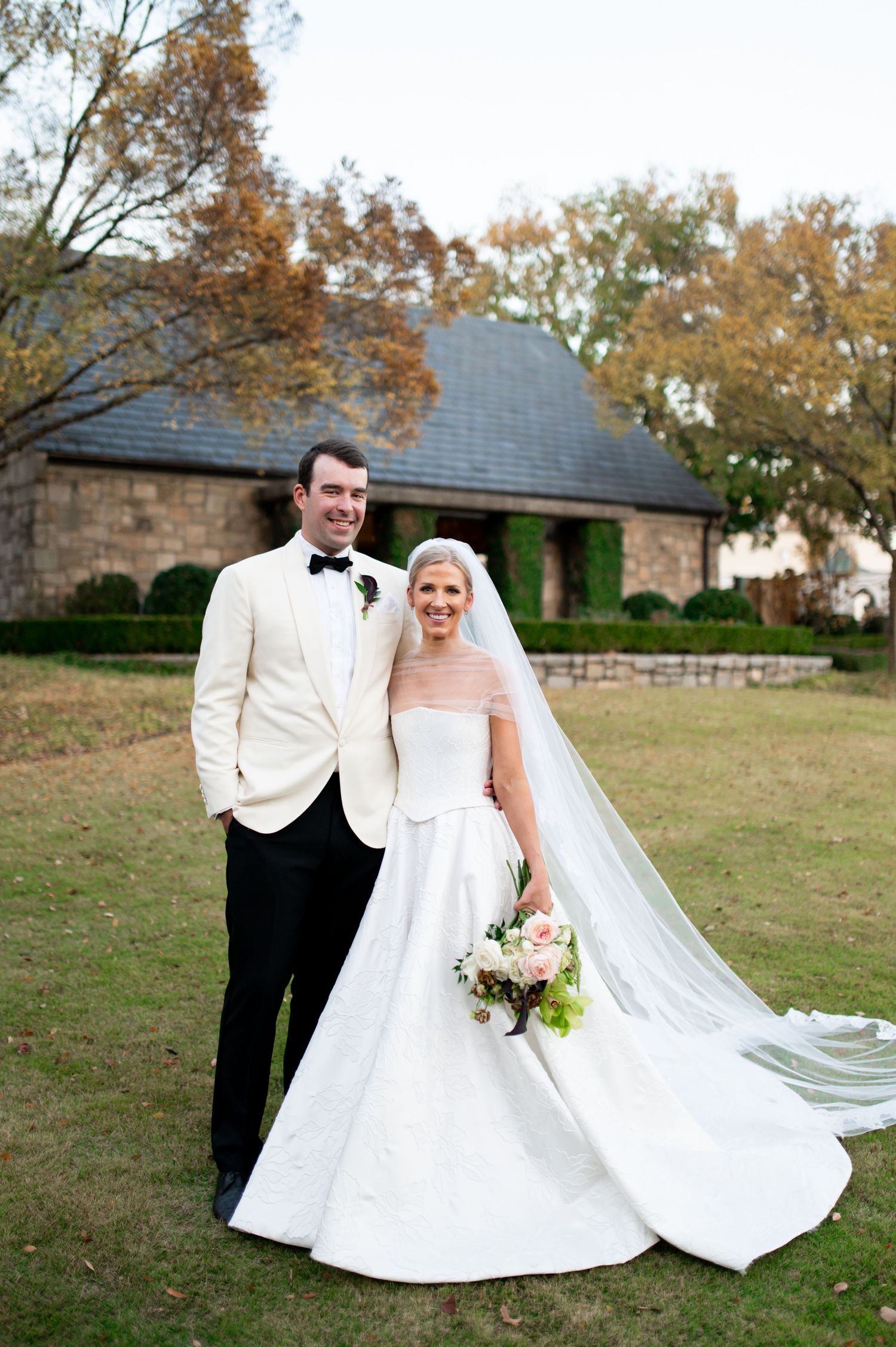 A wedding couple poses playfully in autumn with the bride's dress and veil flowing in the breeze.