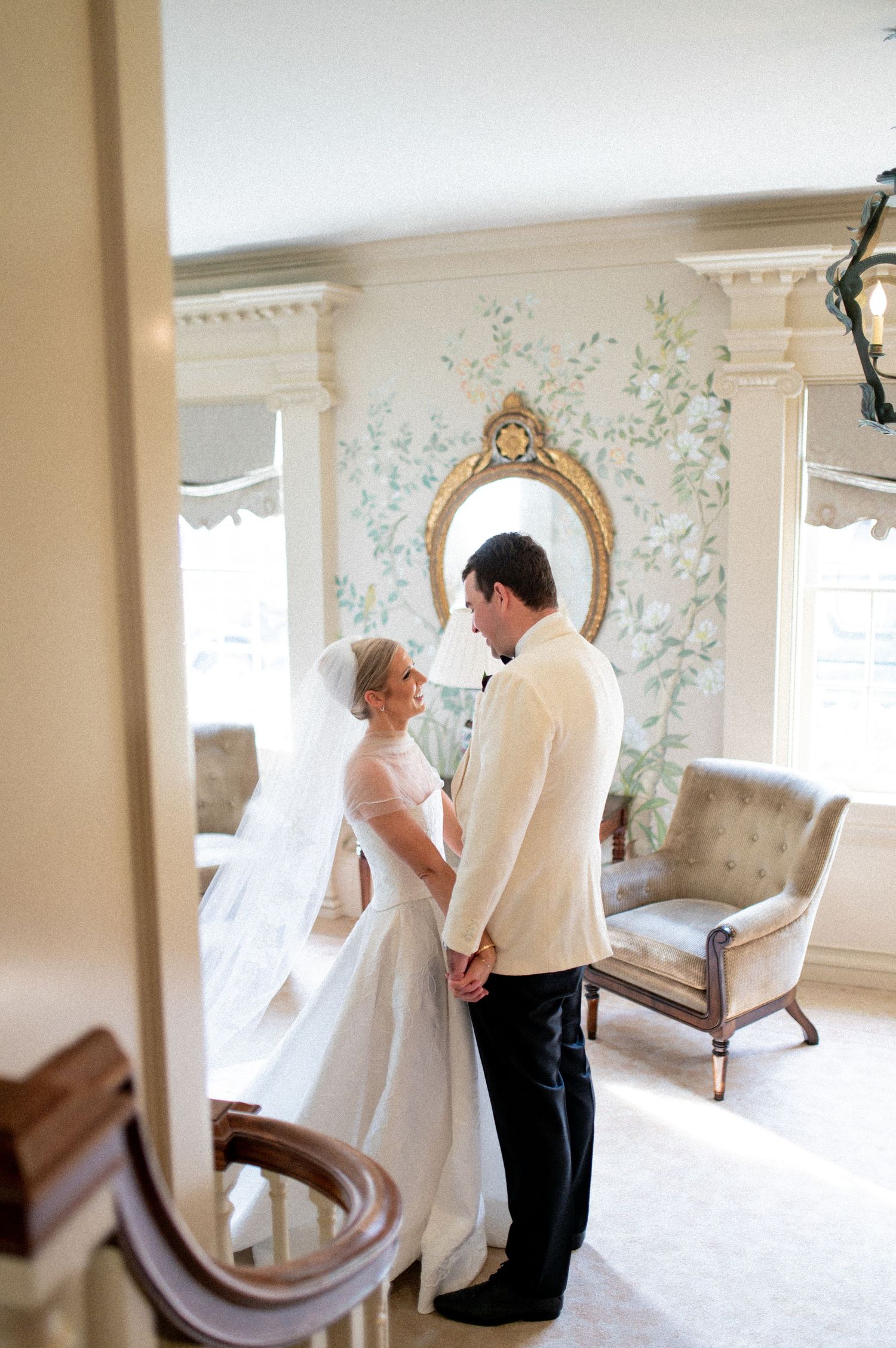 Elegant wedding photos taken in a room with floral wallpaper and antique furniture.