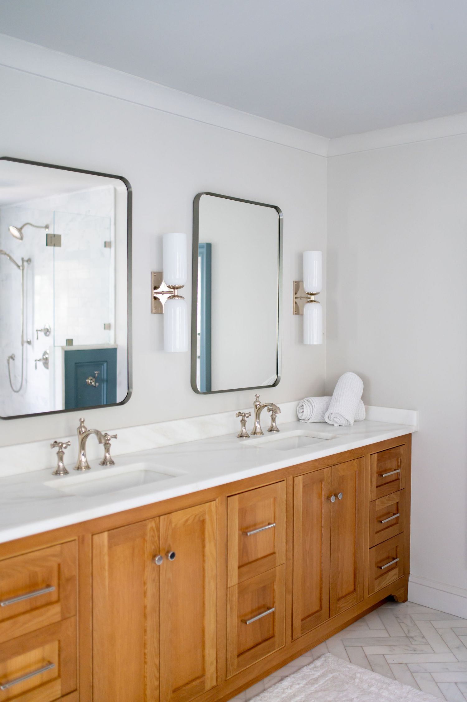 Modern bathroom vanity with warm wood cabinets, white countertop, and black-framed mirror against white walls.