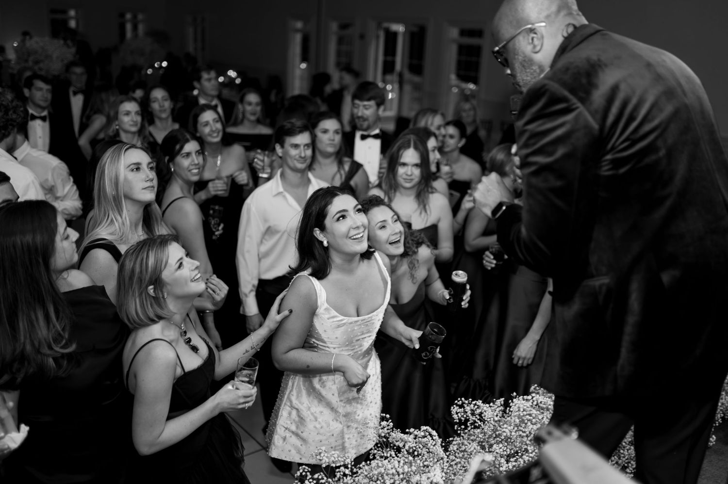 Wedding reception guests dancing and celebrating in dimly lit venue.