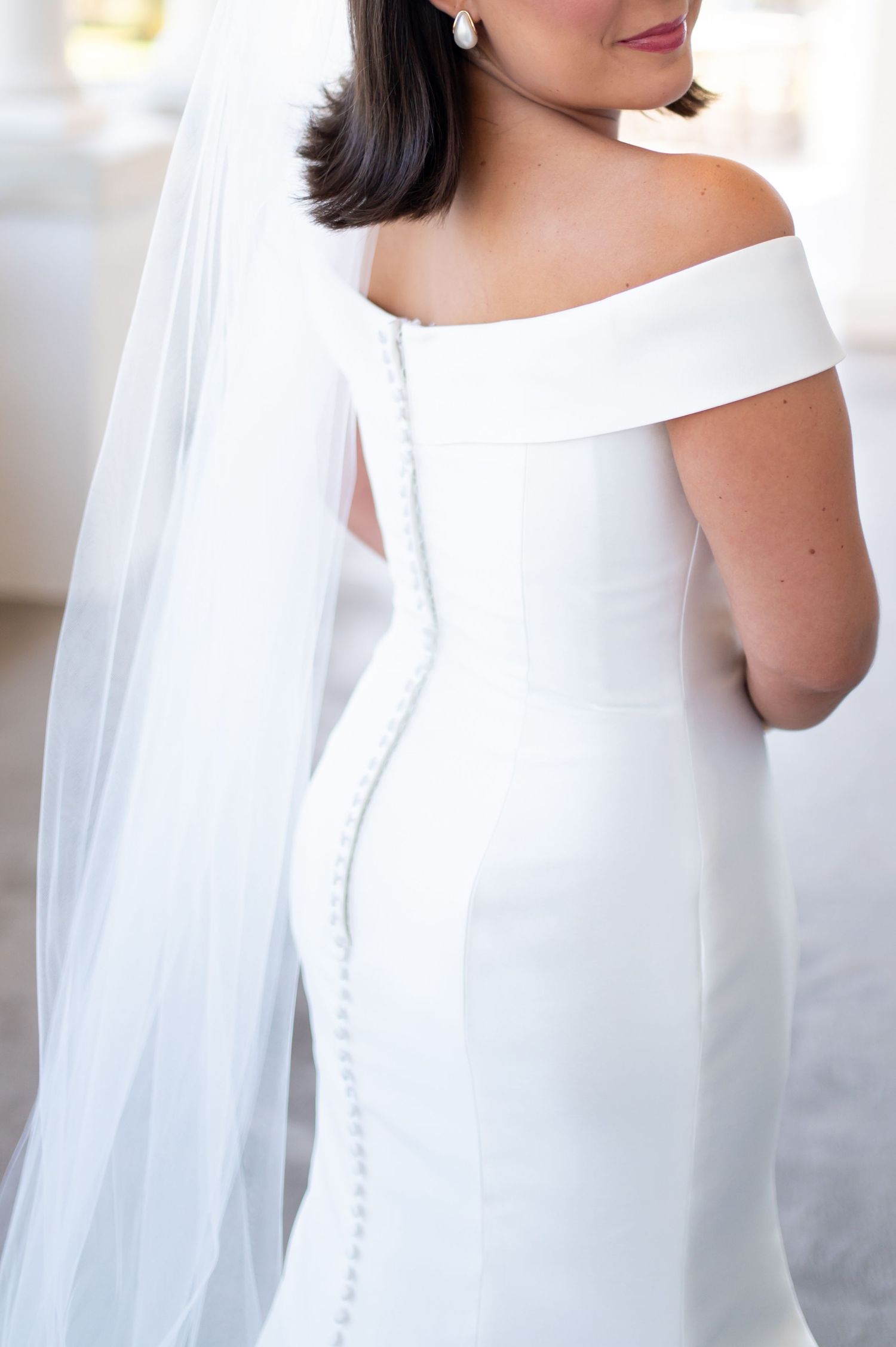 Close-up details of elegant white wedding dress with off-shoulder neckline.