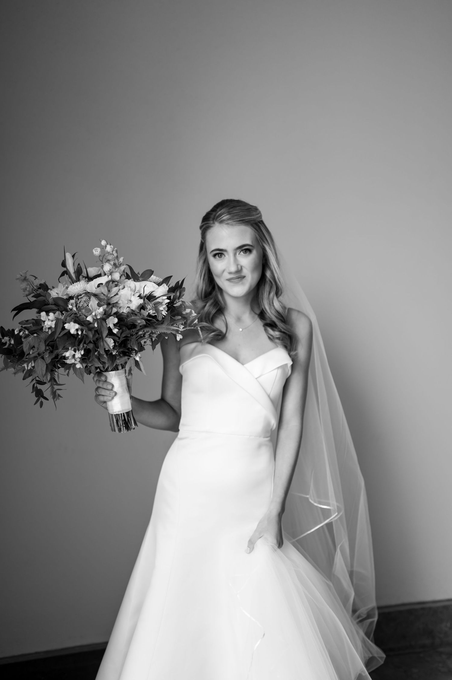 Black and white portrait of bride holding lush floral bouquet in classic wedding gown.