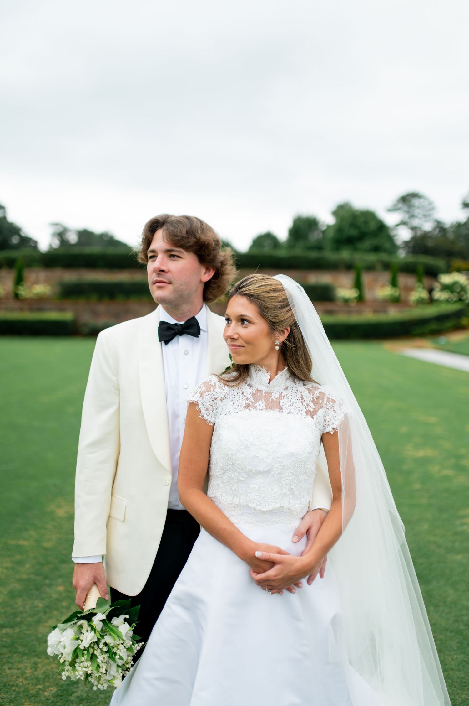 Wedding portrait of couple in white against garden backdrop with classic formal attire.