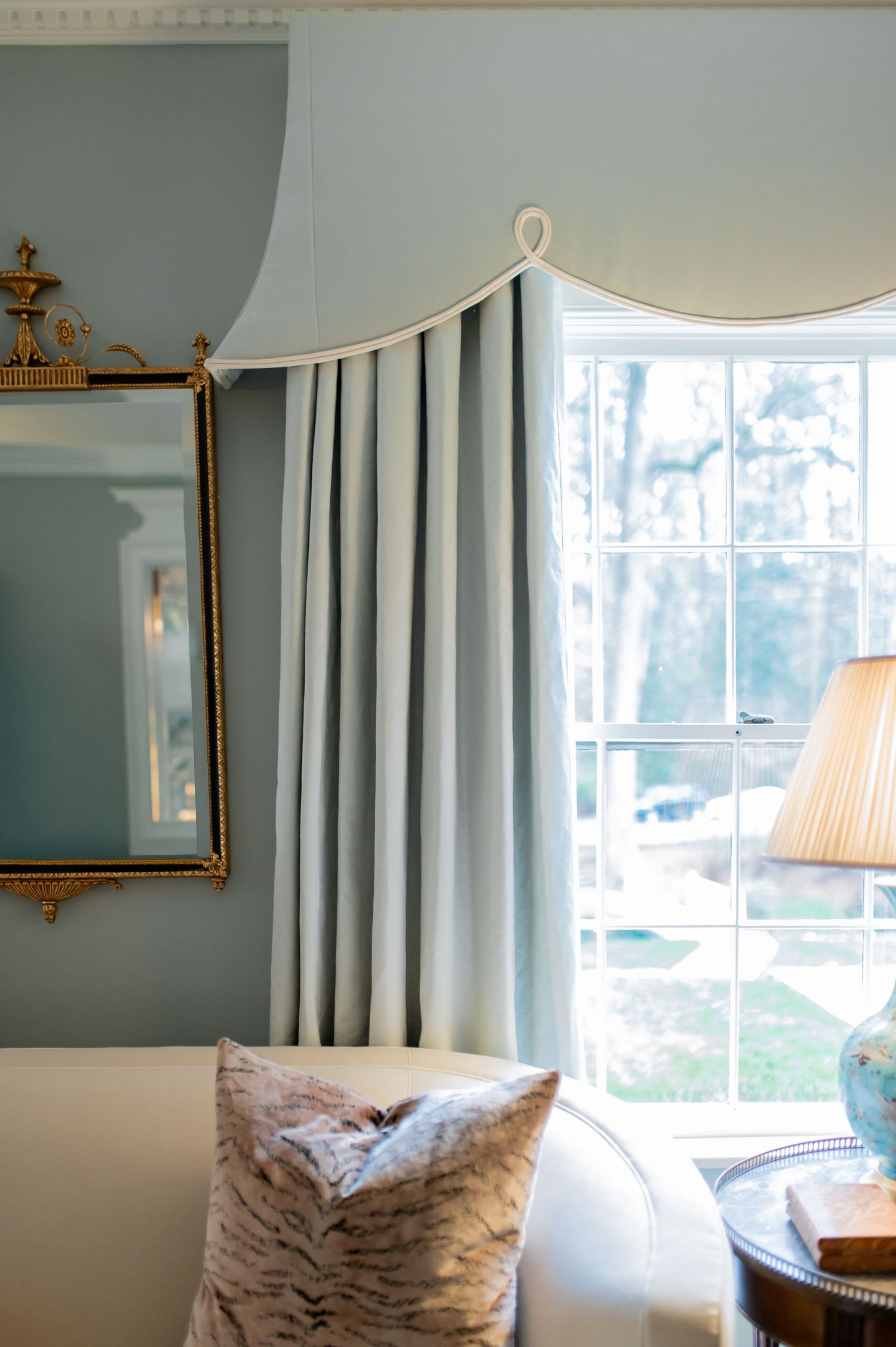 Blue bedroom with elegant curved cornice, light blue drapes, gilded mirror, and tiger print accent pillow.