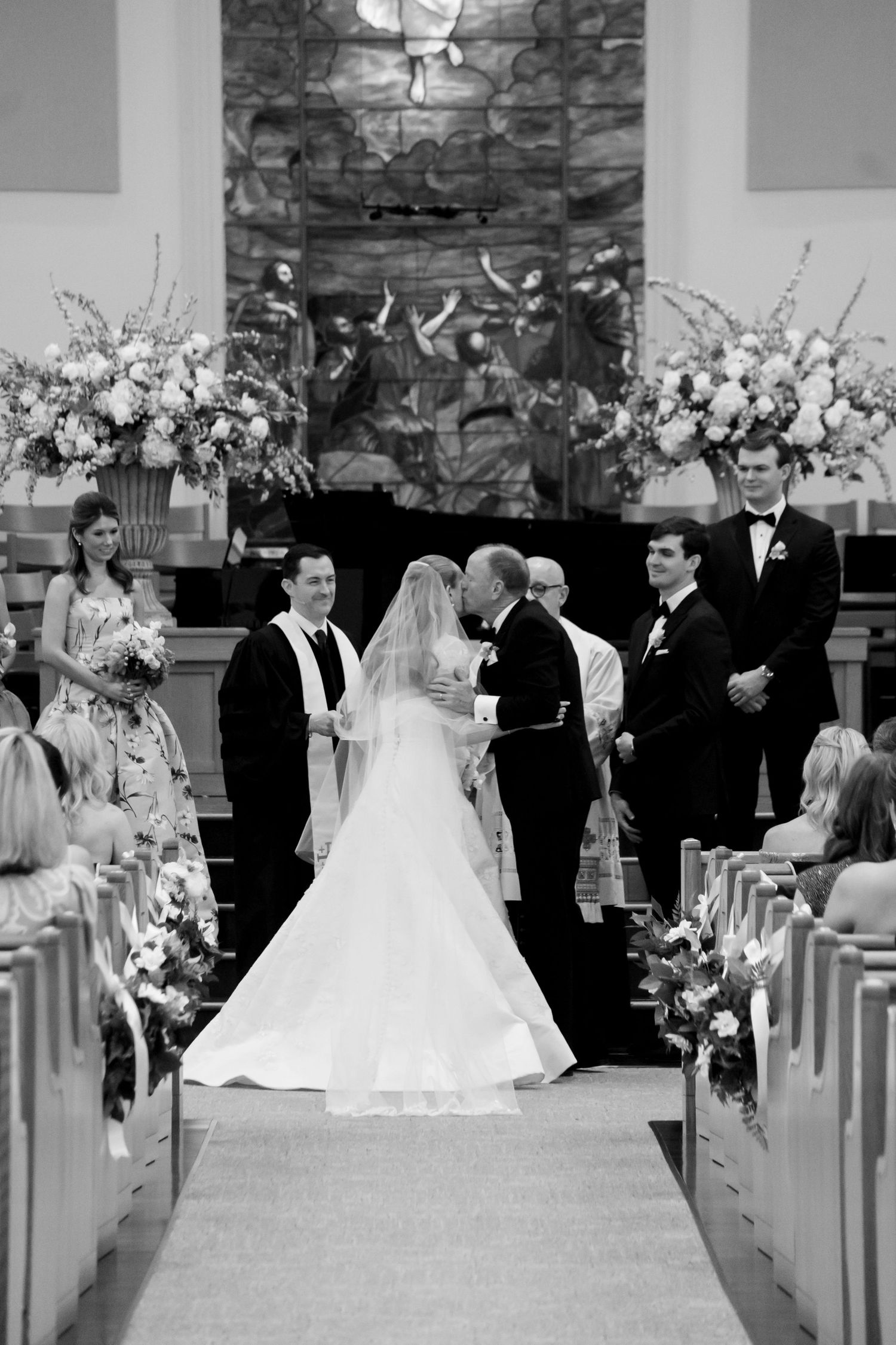 Bride and groom share first kiss at church altar during wedding ceremony in black and white photo.