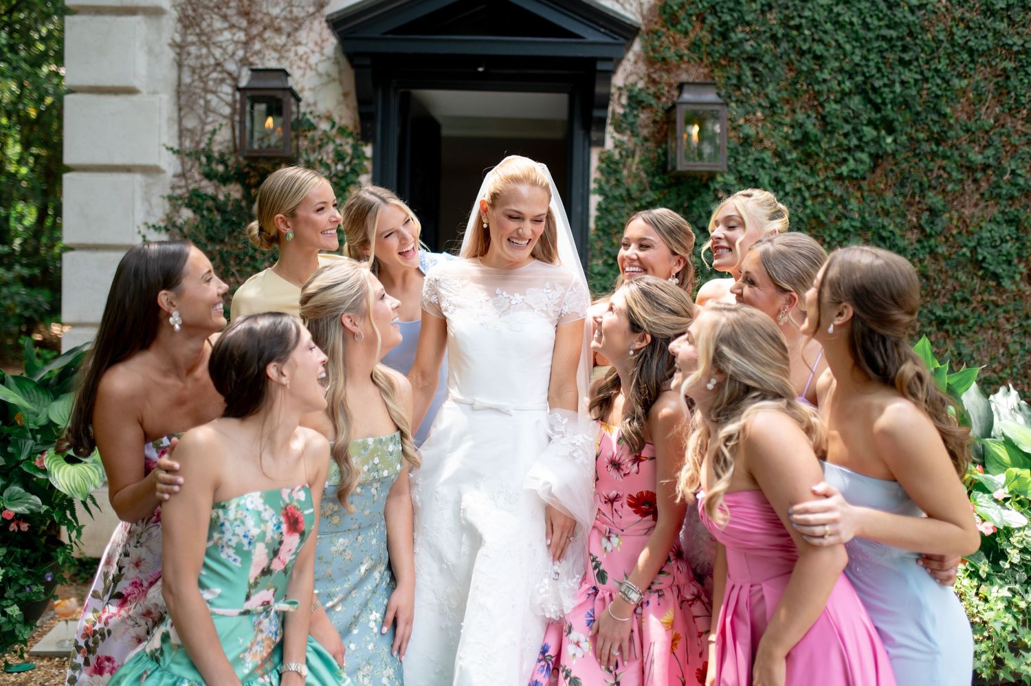 Bride in white gown surrounded by bridesmaids in colorful floral dresses outdoors at wedding celebration.