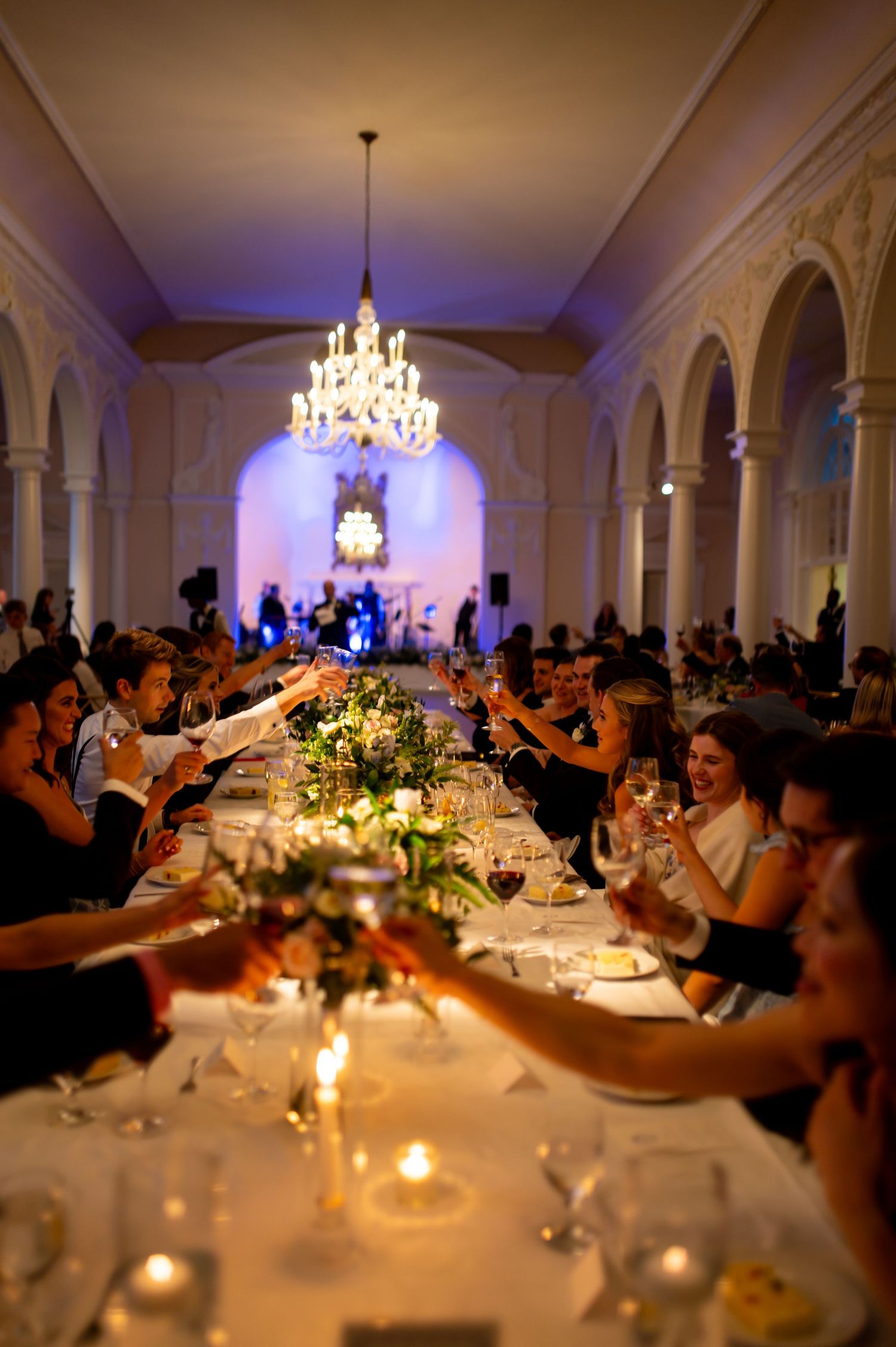 Evening wedding reception with guests dining at candlelit tables under crystal chandeliers.