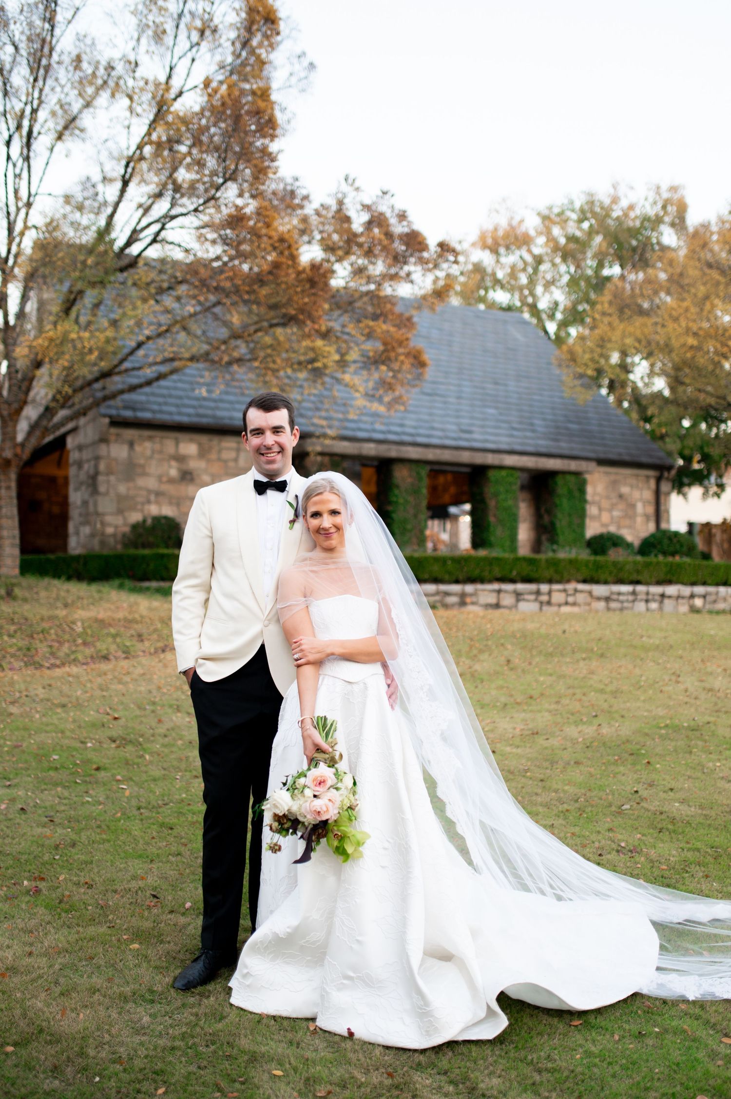 Wedding couple photographed on autumn lawn with brick building in background.