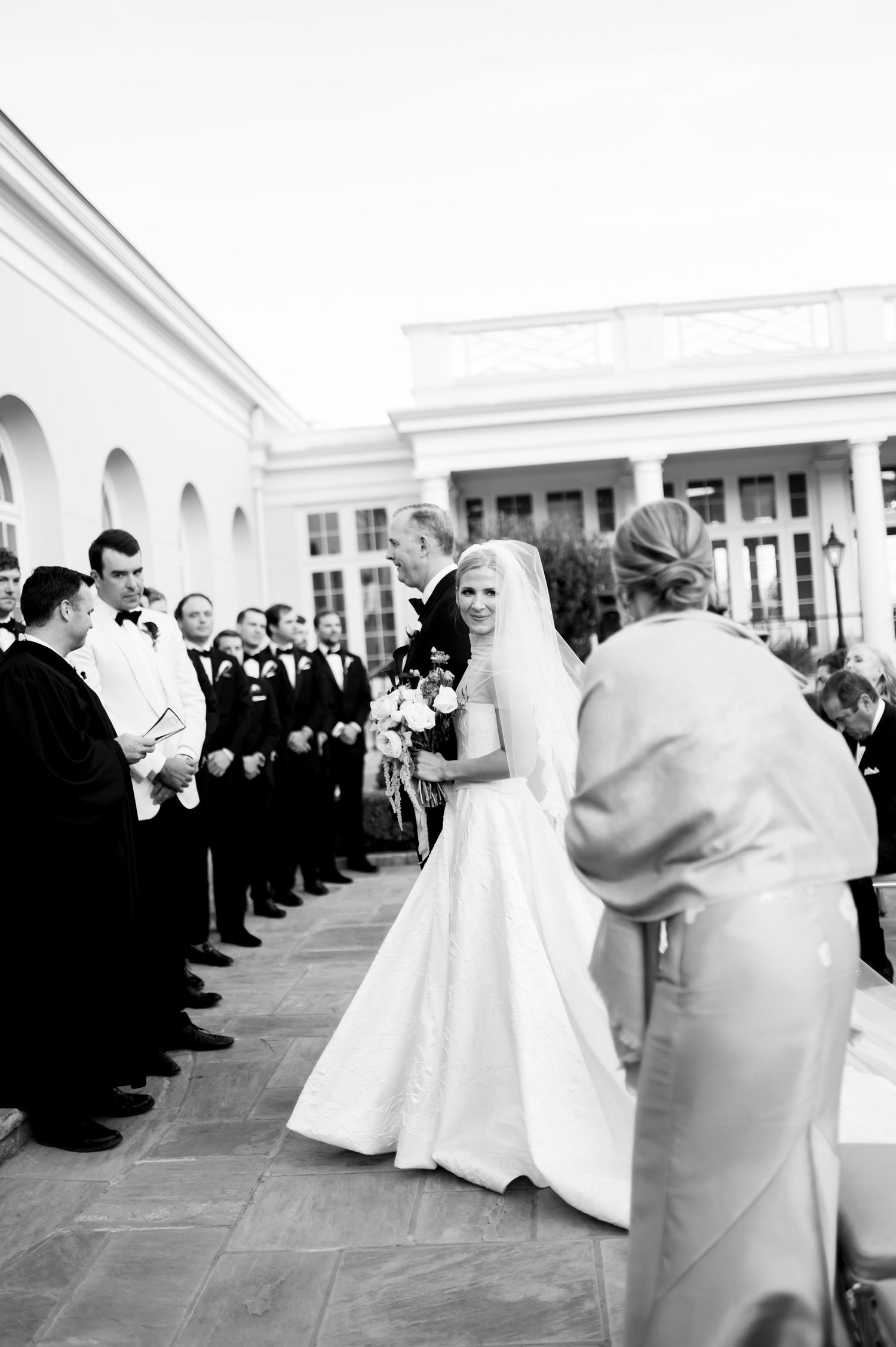 Black and white photo of wedding party processional on stone courtyard.
