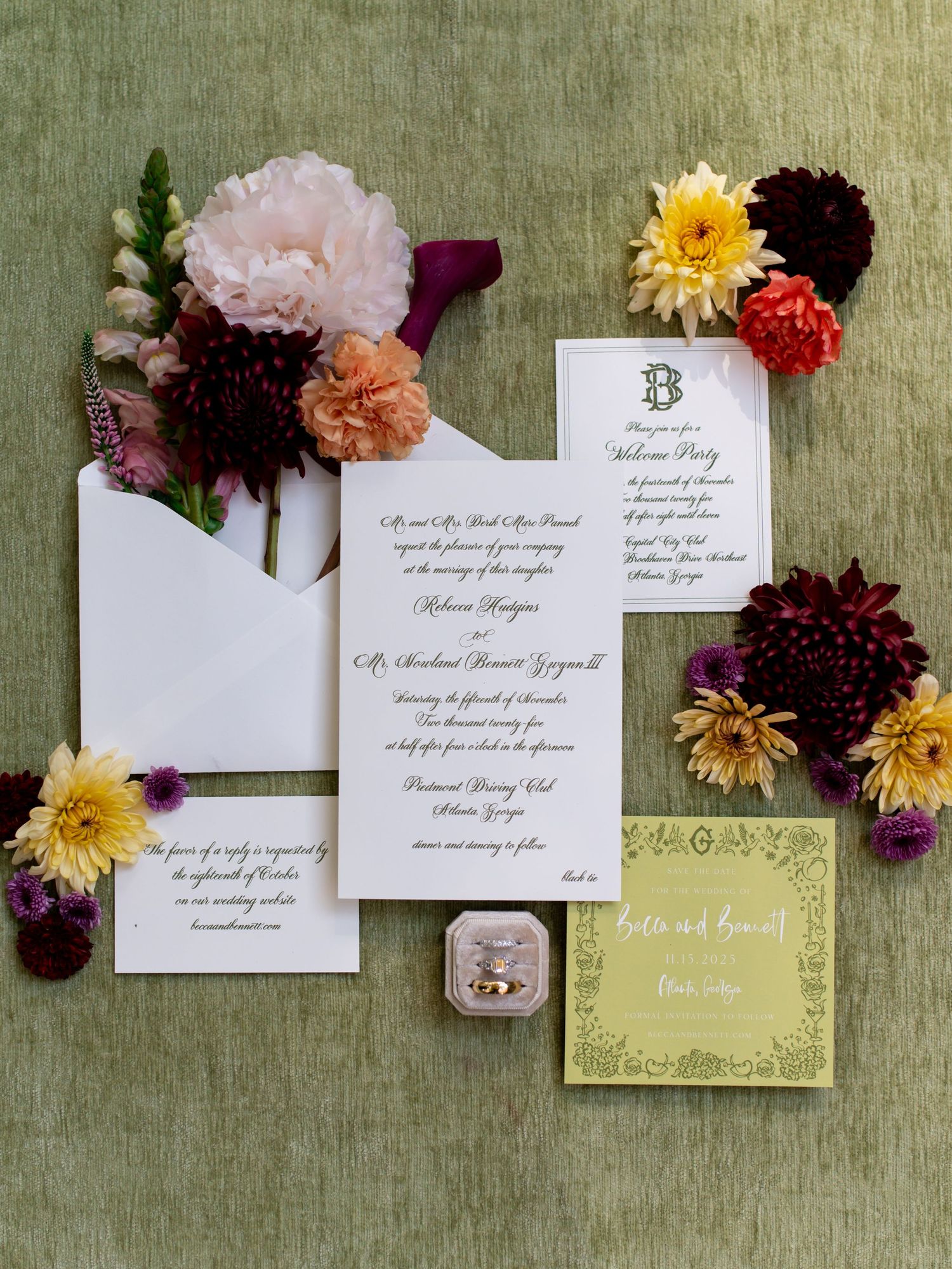 Elegant wedding invitation suite with burgundy and yellow flowers arranged on sage green linen background.