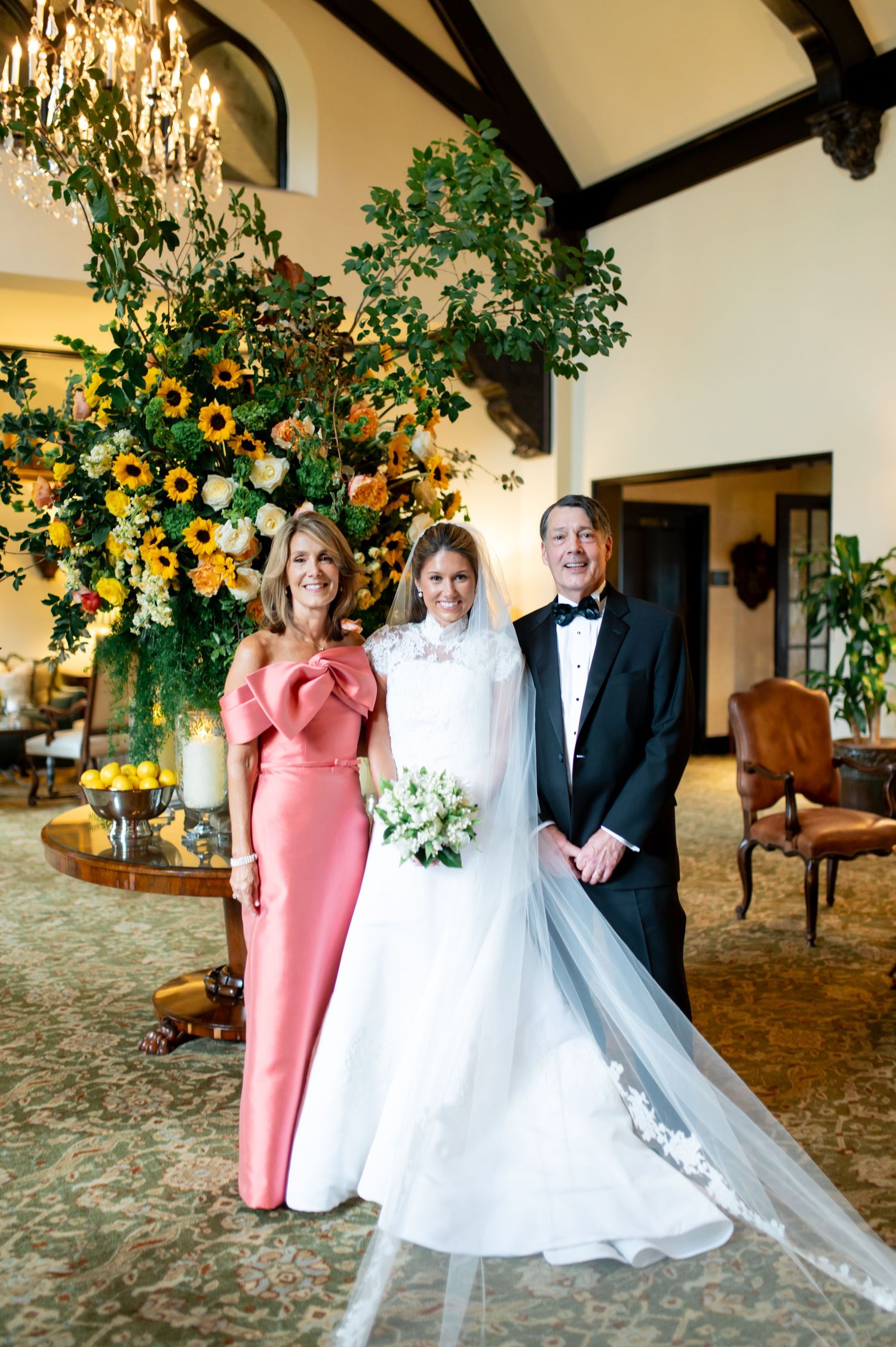 A wedding party poses in formal attire with sunflower and greenery decorations in the background.
