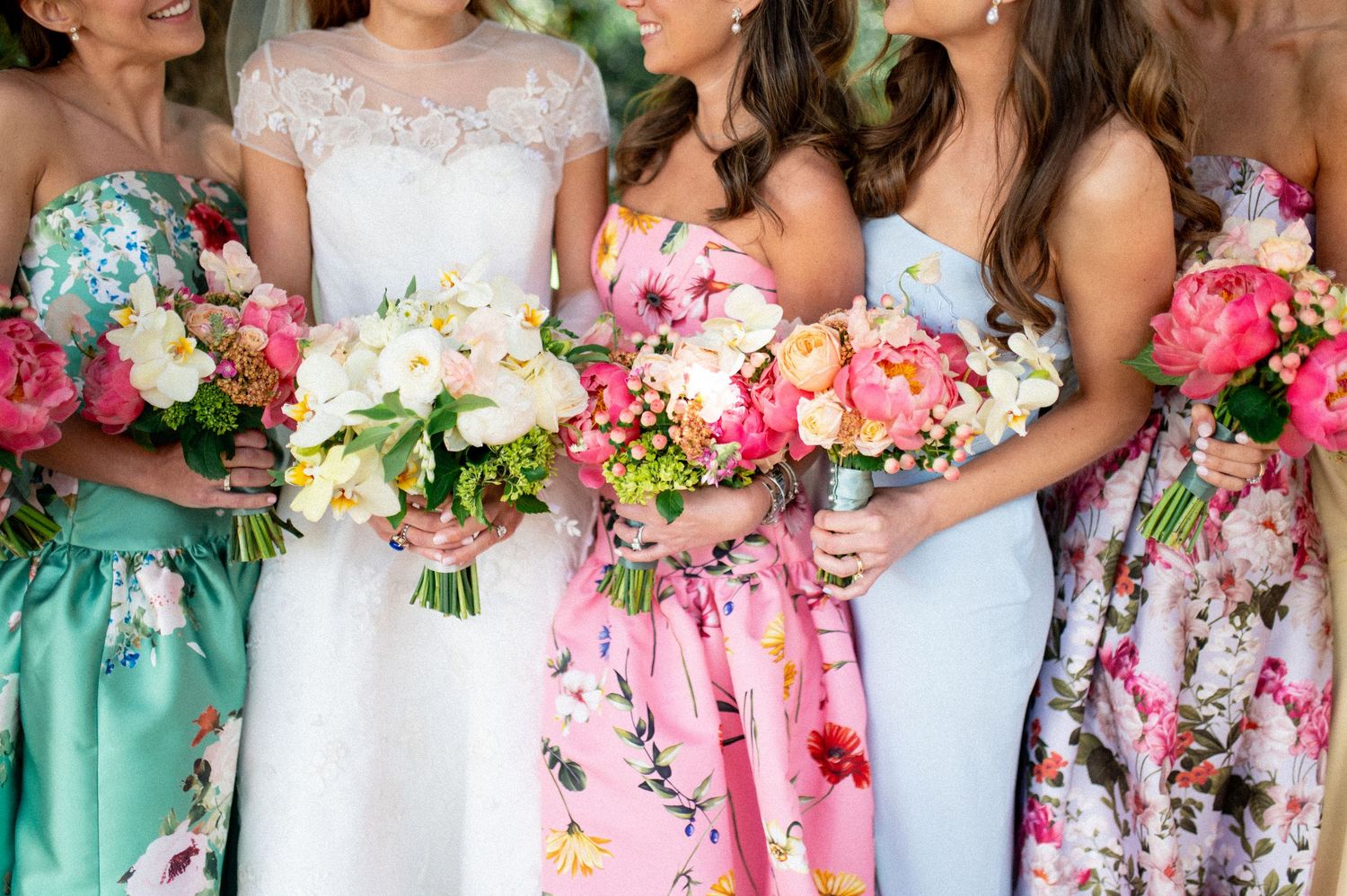 Bride and bridesmaids in colorful floral dresses holding vibrant pink and white bouquets.