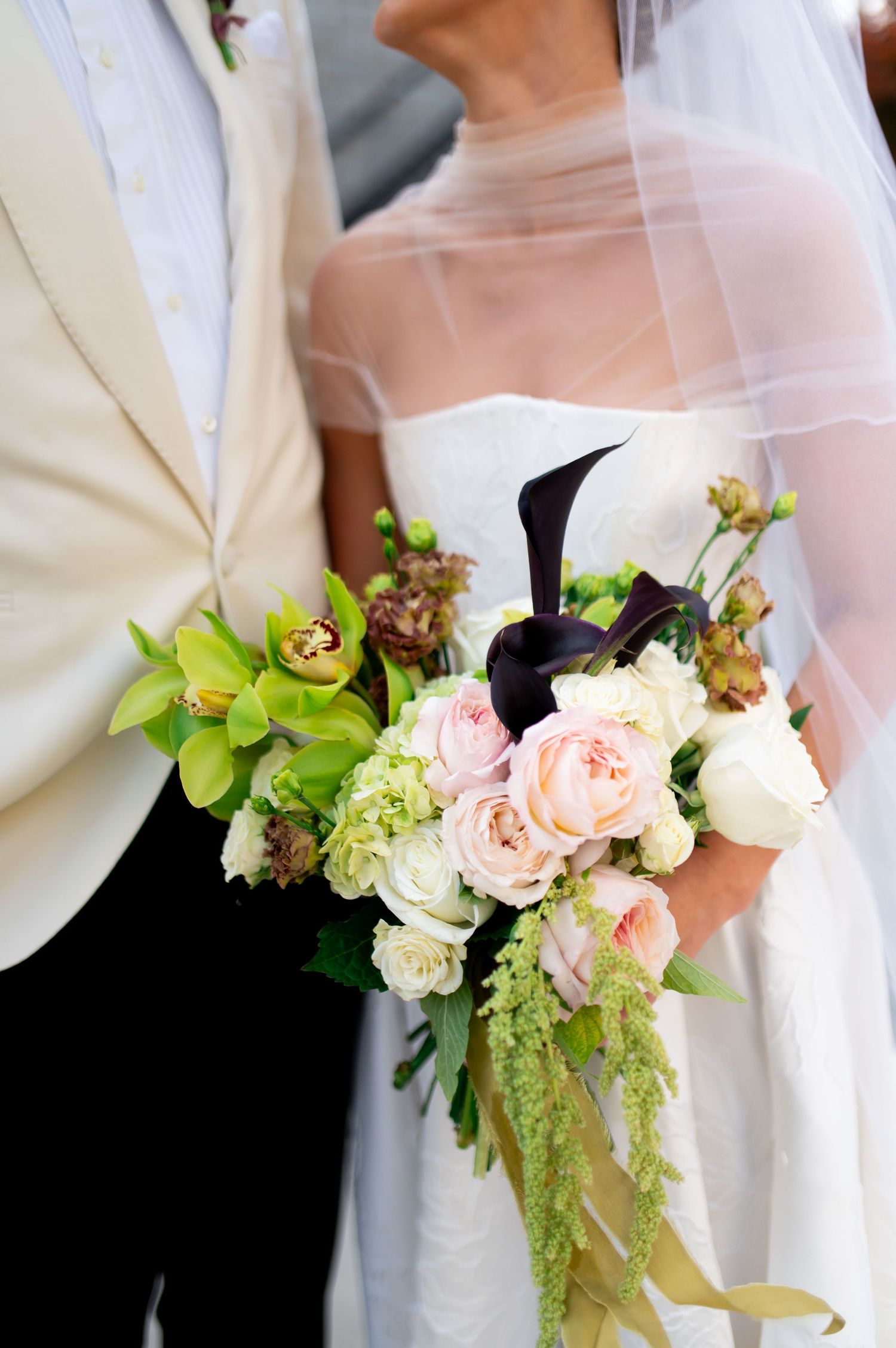Wedding bouquet featuring pink roses, green orchids and white flowers with flowing ribbons.