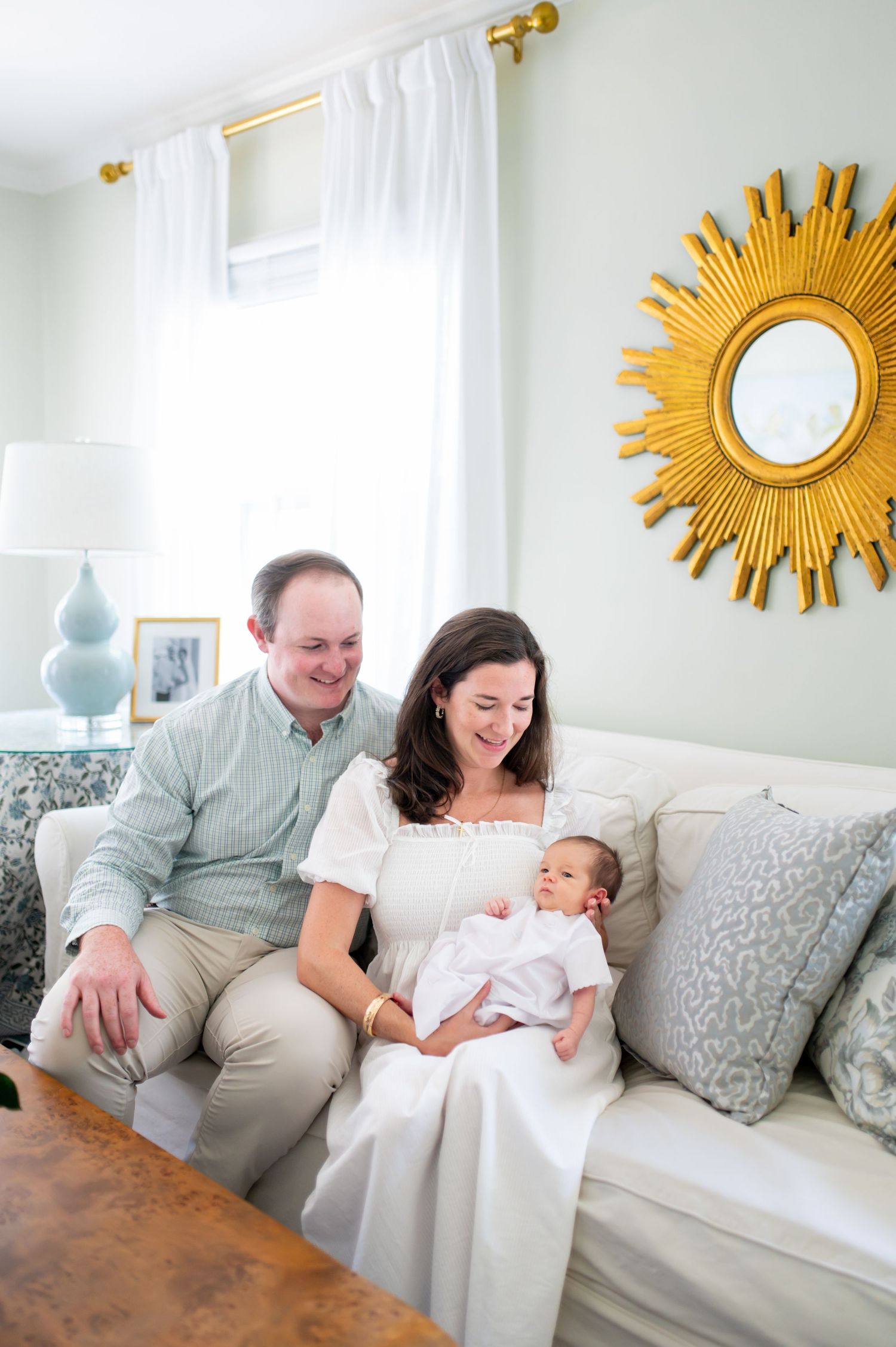 A bright living room scene with a gold sunburst mirror and family moment on a white couch.