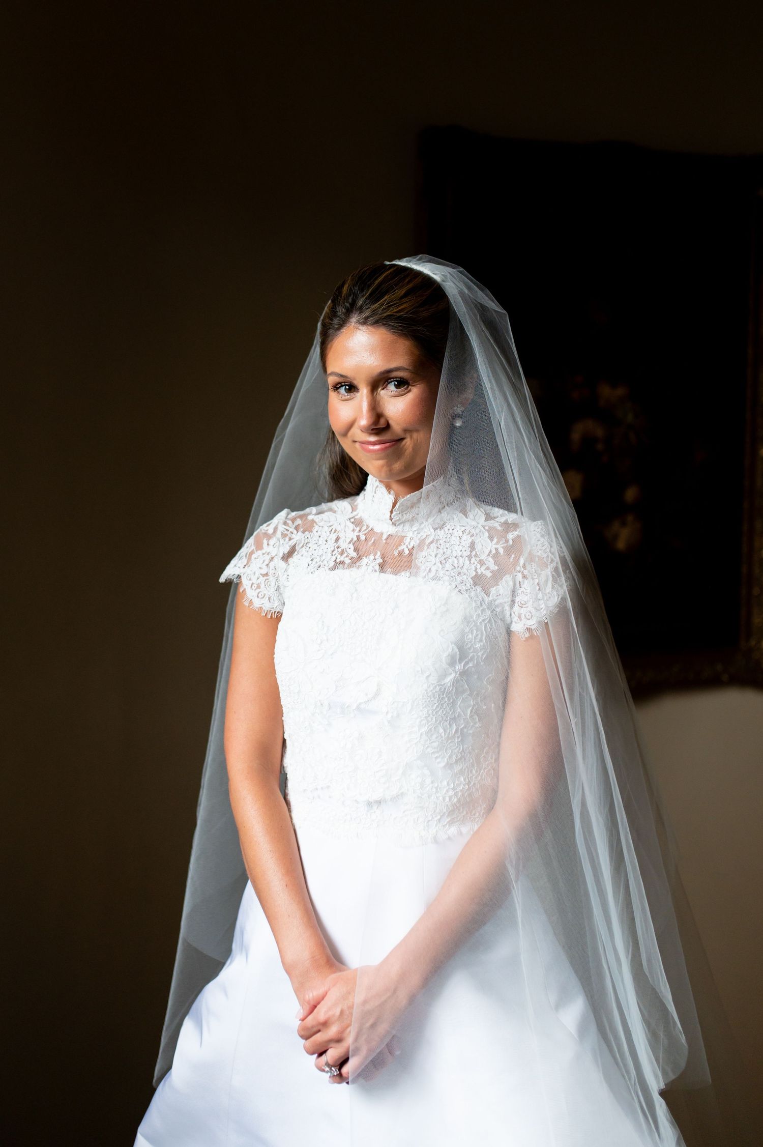 Classic bridal portrait featuring lace dress and veil in dramatic lighting.