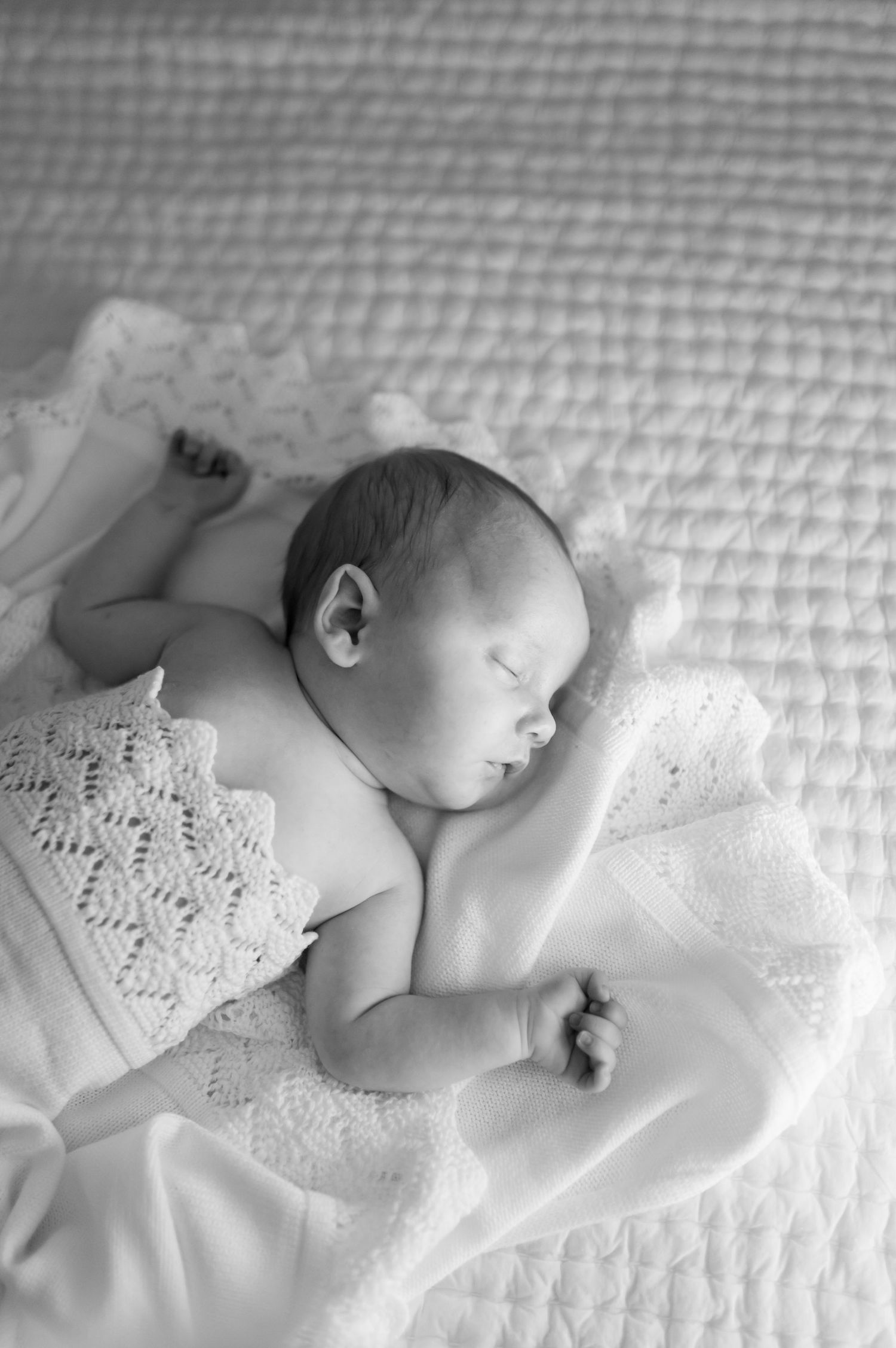 Black and white photo series showing a sleeping newborn baby lying on white textured bedding with delicate lace details.