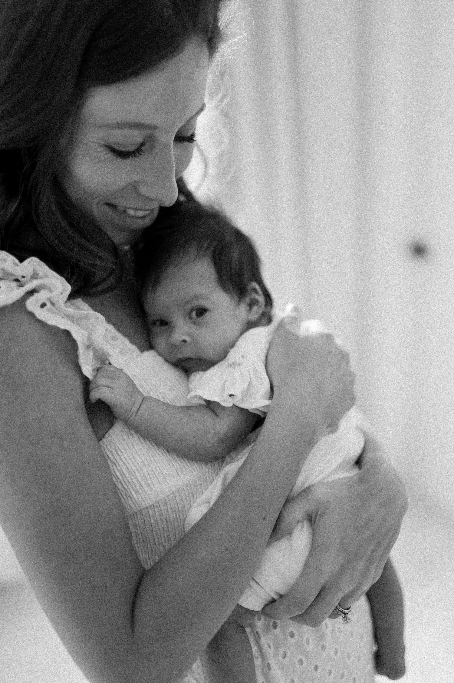 An intimate black and white portrait of a mother cradling her newborn baby.