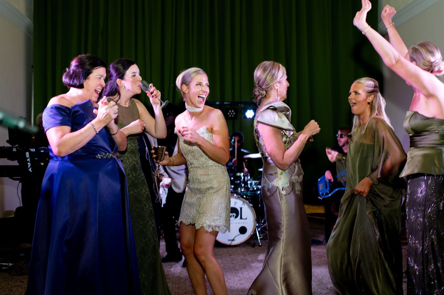 Wedding guests dancing and celebrating at an evening reception with dark backdrop.