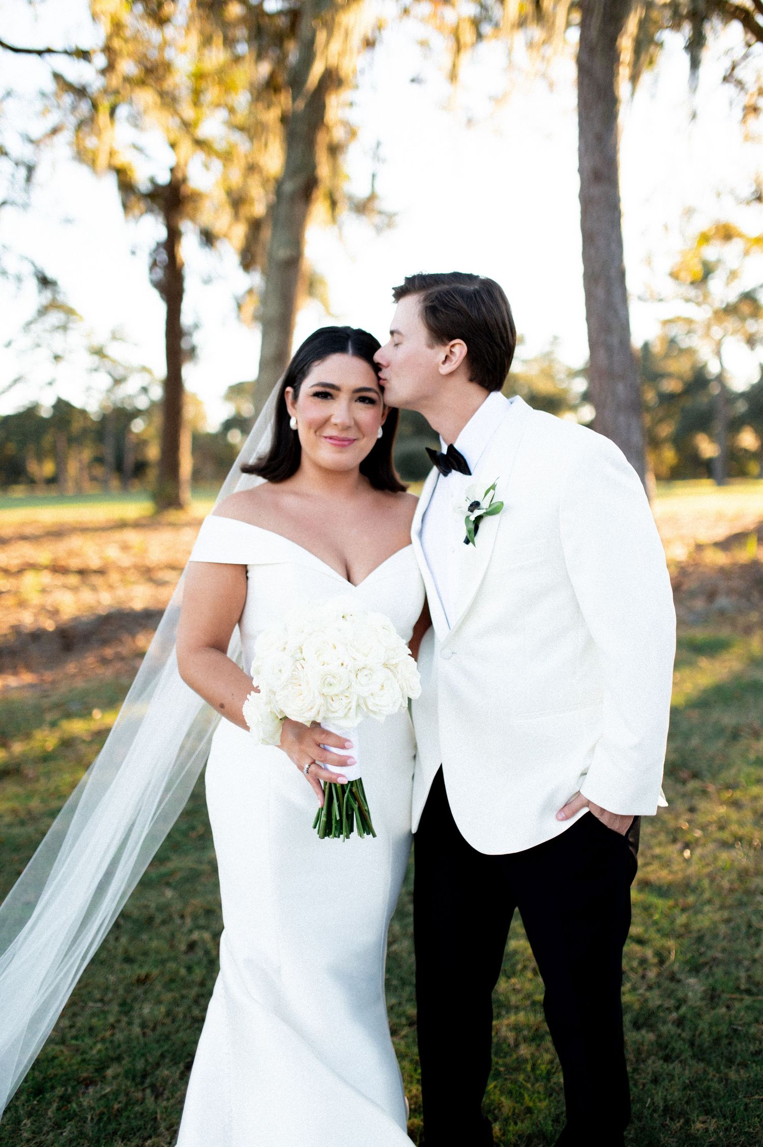Elegant wedding couple poses outdoors at sunset with the bride wearing a flowing white gown and veil.