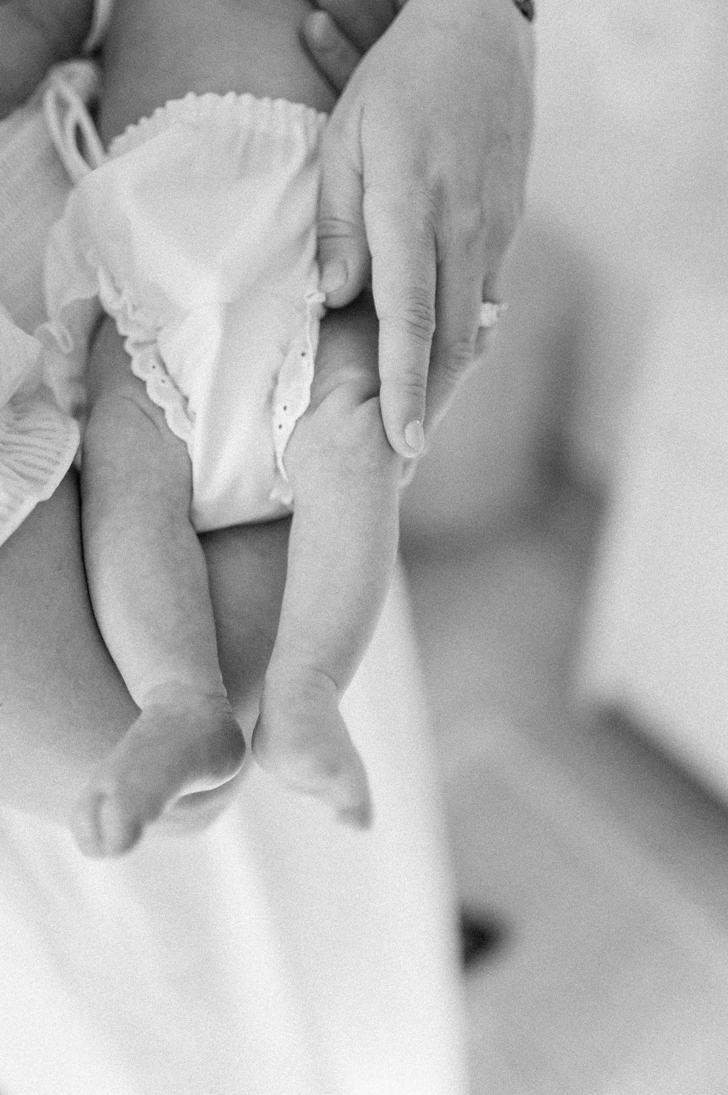Black and white photo showing gentle hands holding a baby's legs wearing a white cloth diaper.