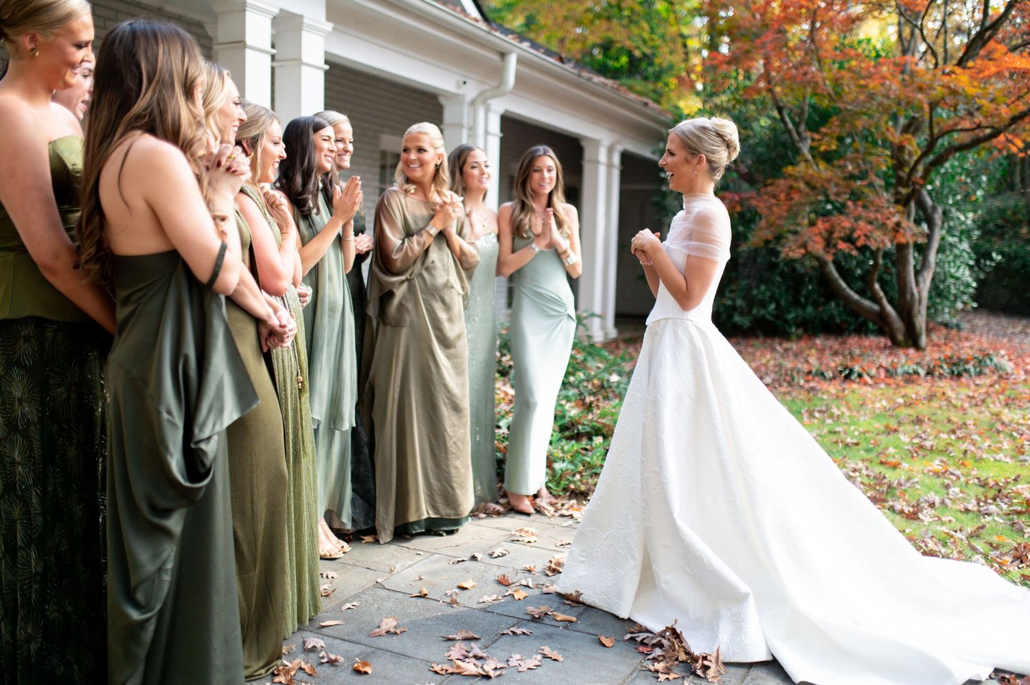 Emotional wedding party first look moment on a white columned porch surrounded by fall colors.