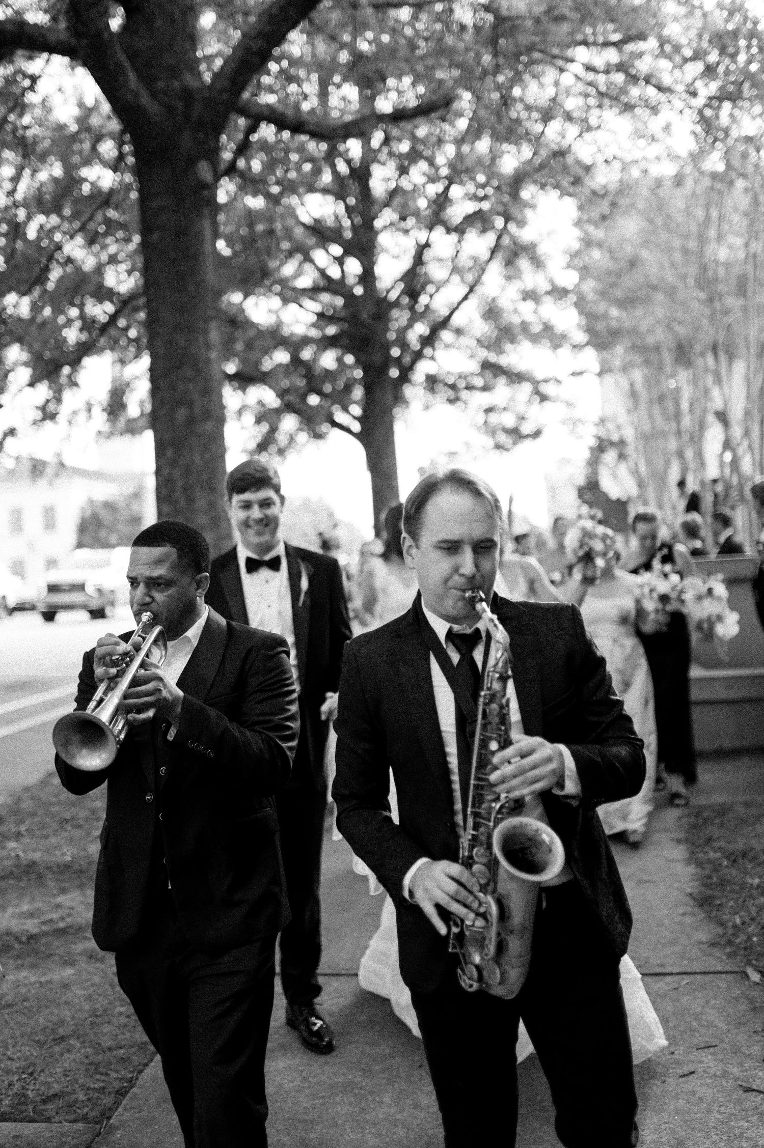 Black and white photo of jazz musicians leading a wedding second line parade on a sidewalk.