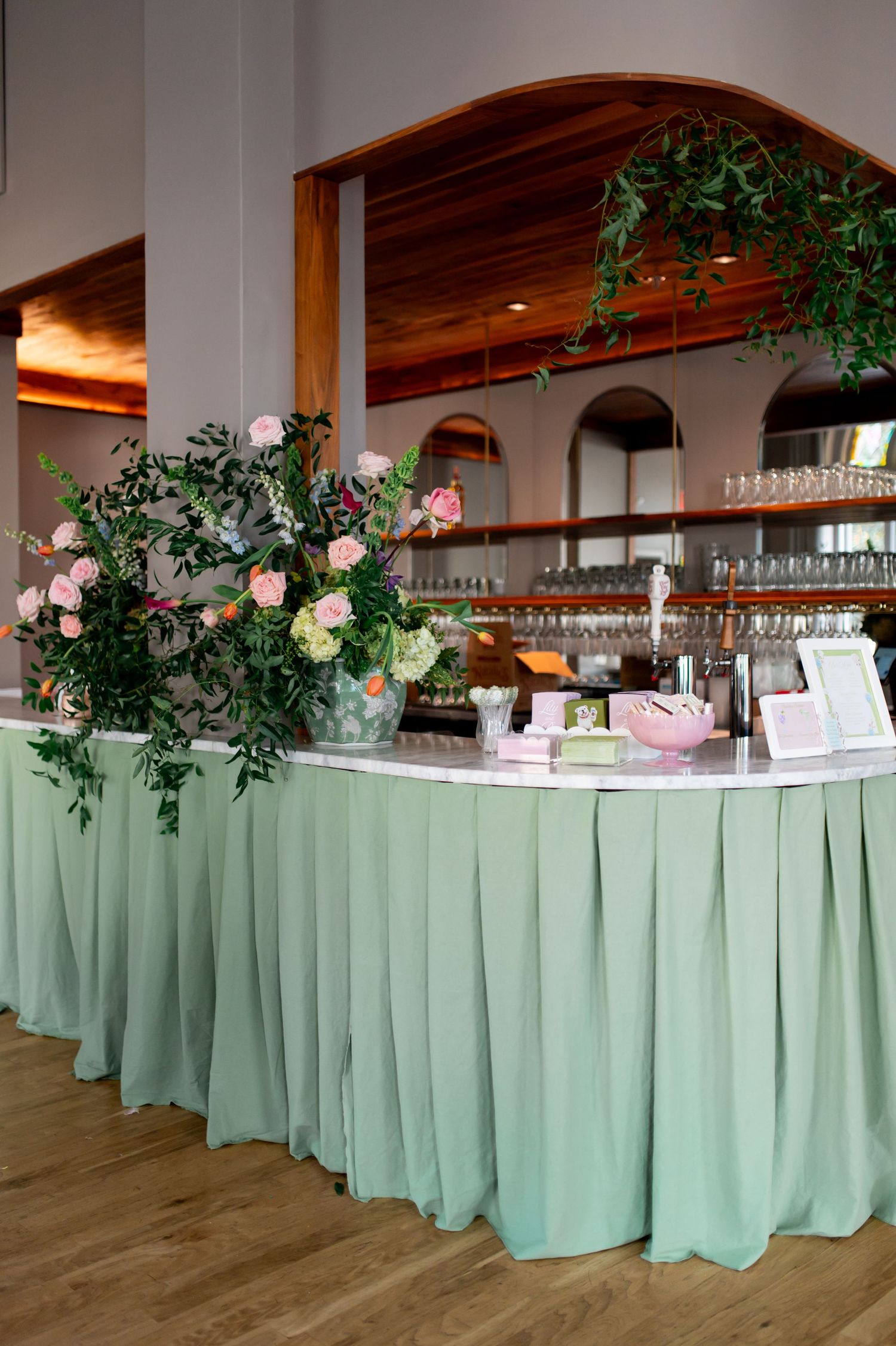 Mint green skirted bar decorated with pink roses and greenery at wedding reception venue.