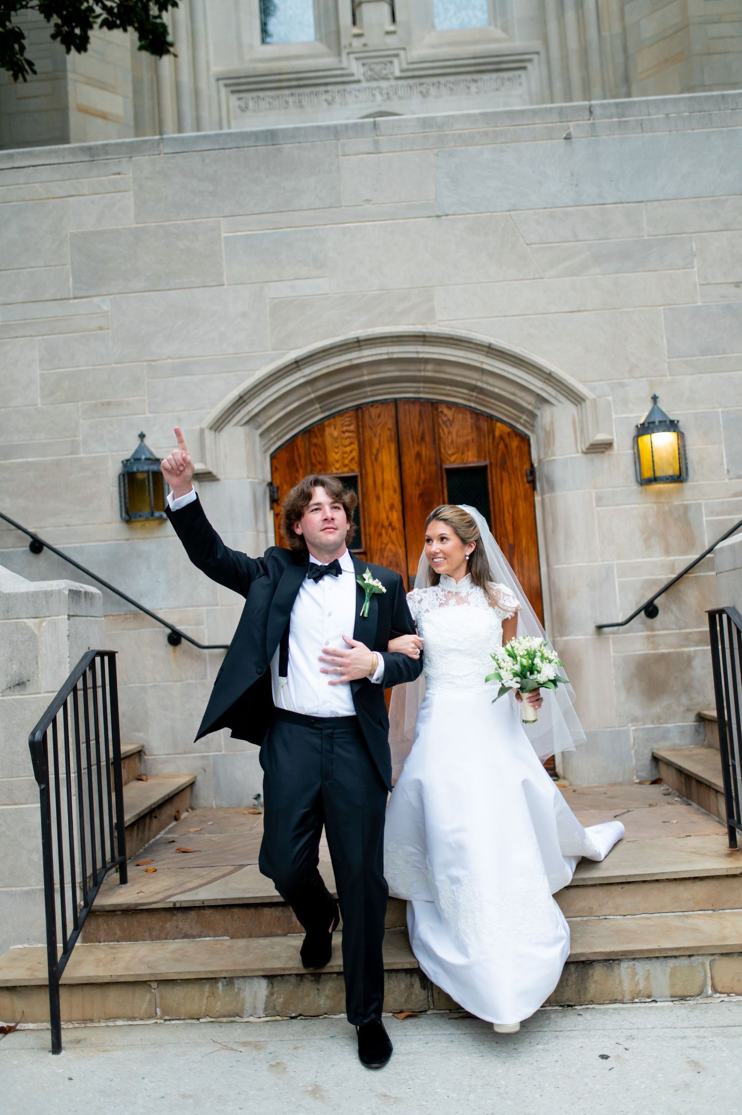 Wedding couple performs fun jumping poses on church steps.