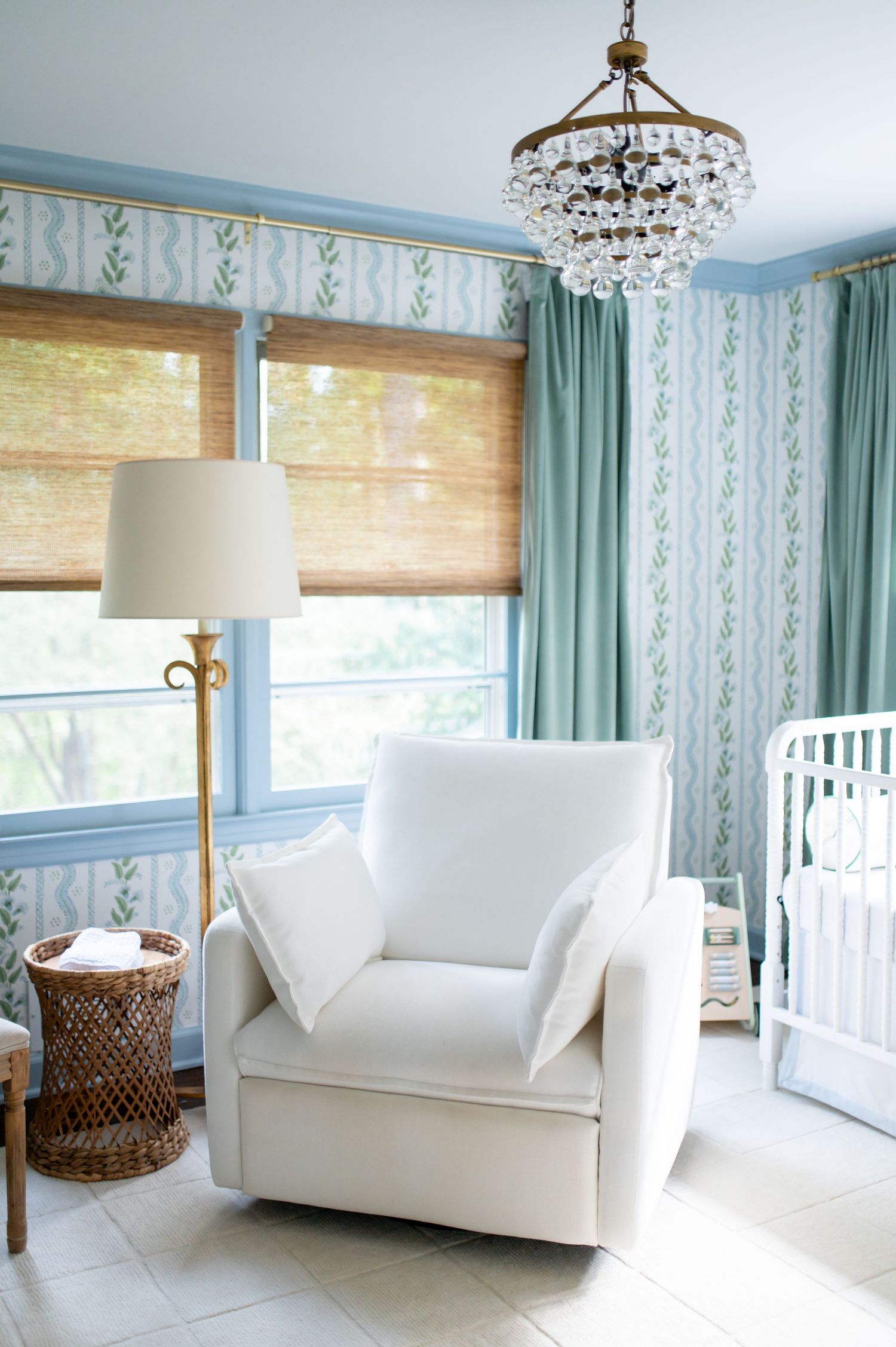 Modern living room interior with white loveseat, turquoise curtains, bamboo shades and crystal chandelier lighting.