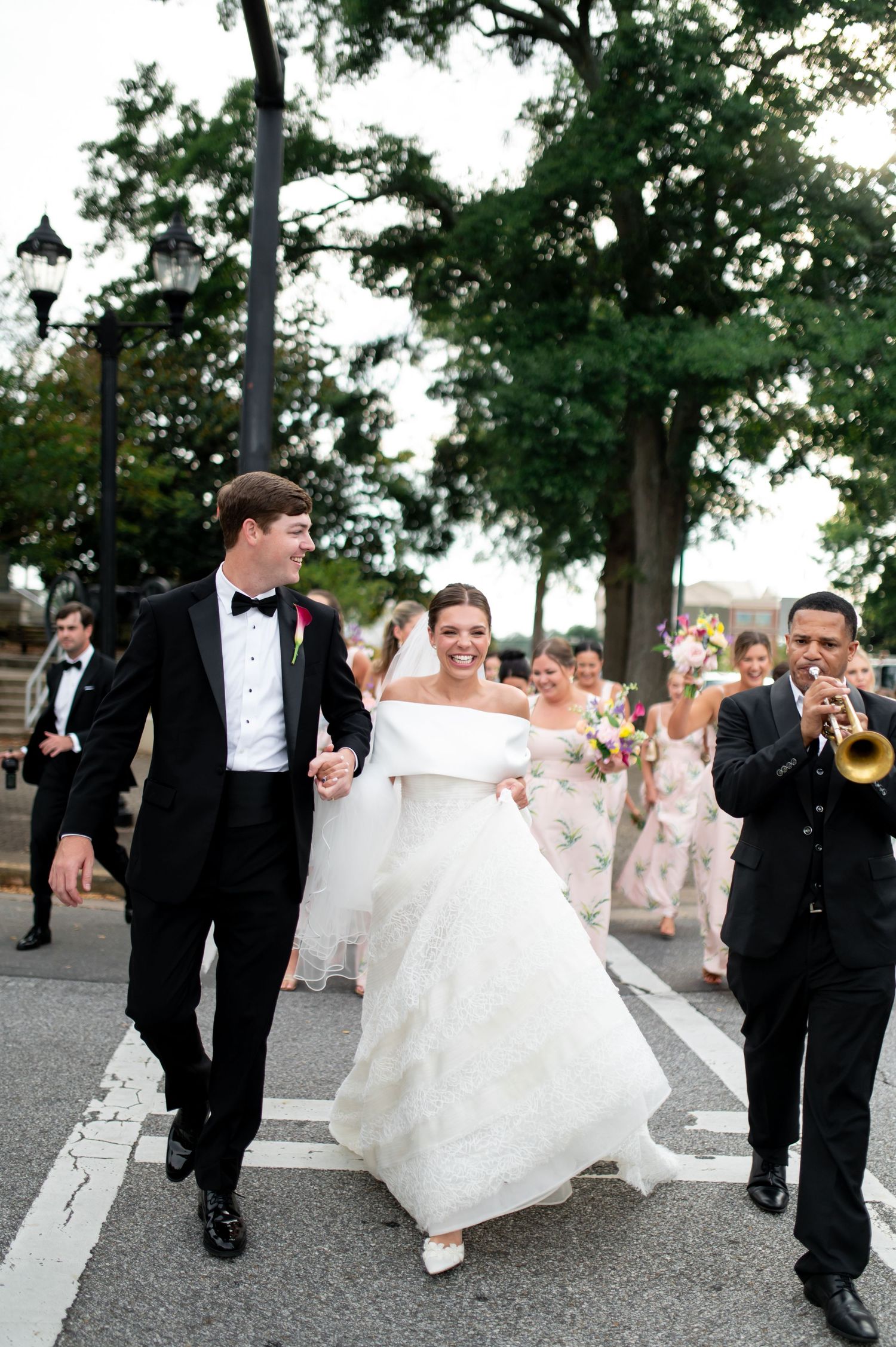 Joyful bride and groom walk hand-in-hand during a New Orleans second line wedding parade with trumpet player.