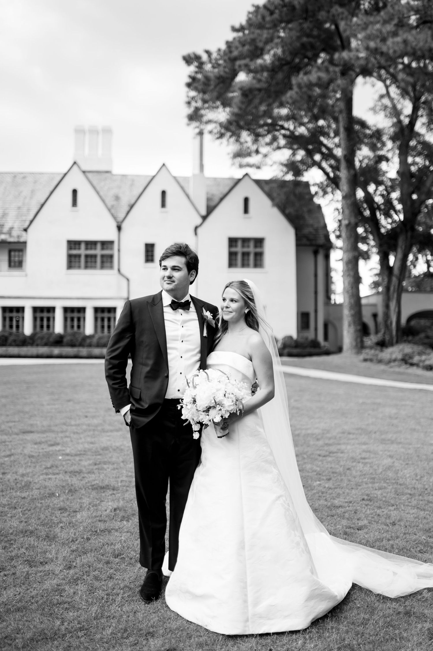 Black and white wedding photos captured on a lawn with white buildings in the background.