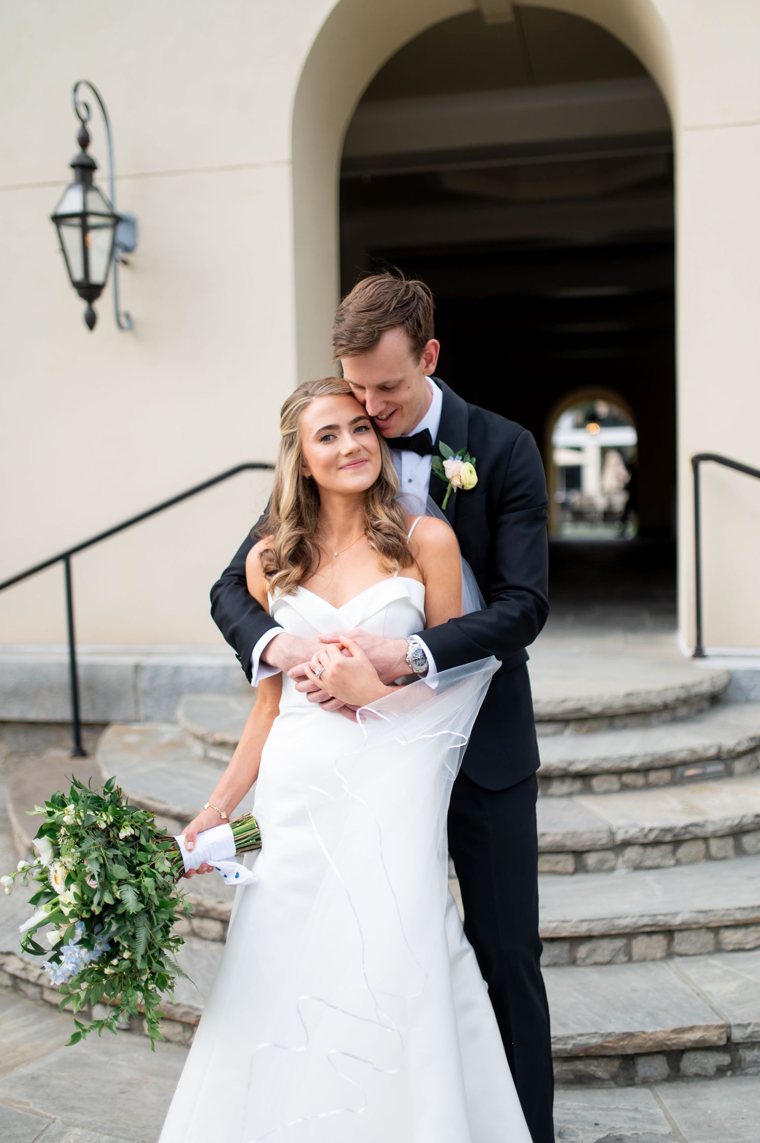 Newlyweds share an intimate moment outside a stone archway with greenery.
