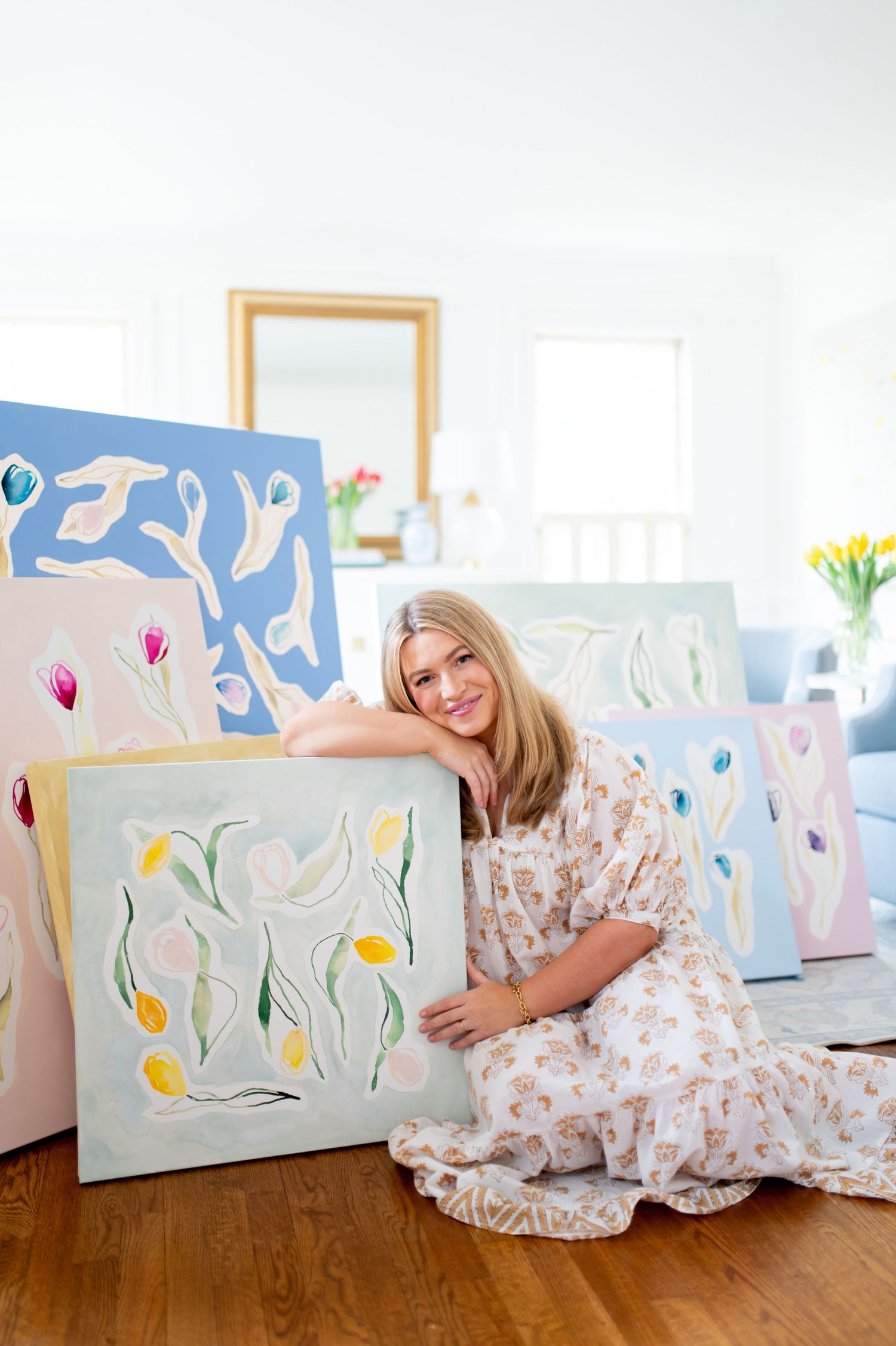 Woman in white dress poses with colorful abstract artwork in bright gallery space.