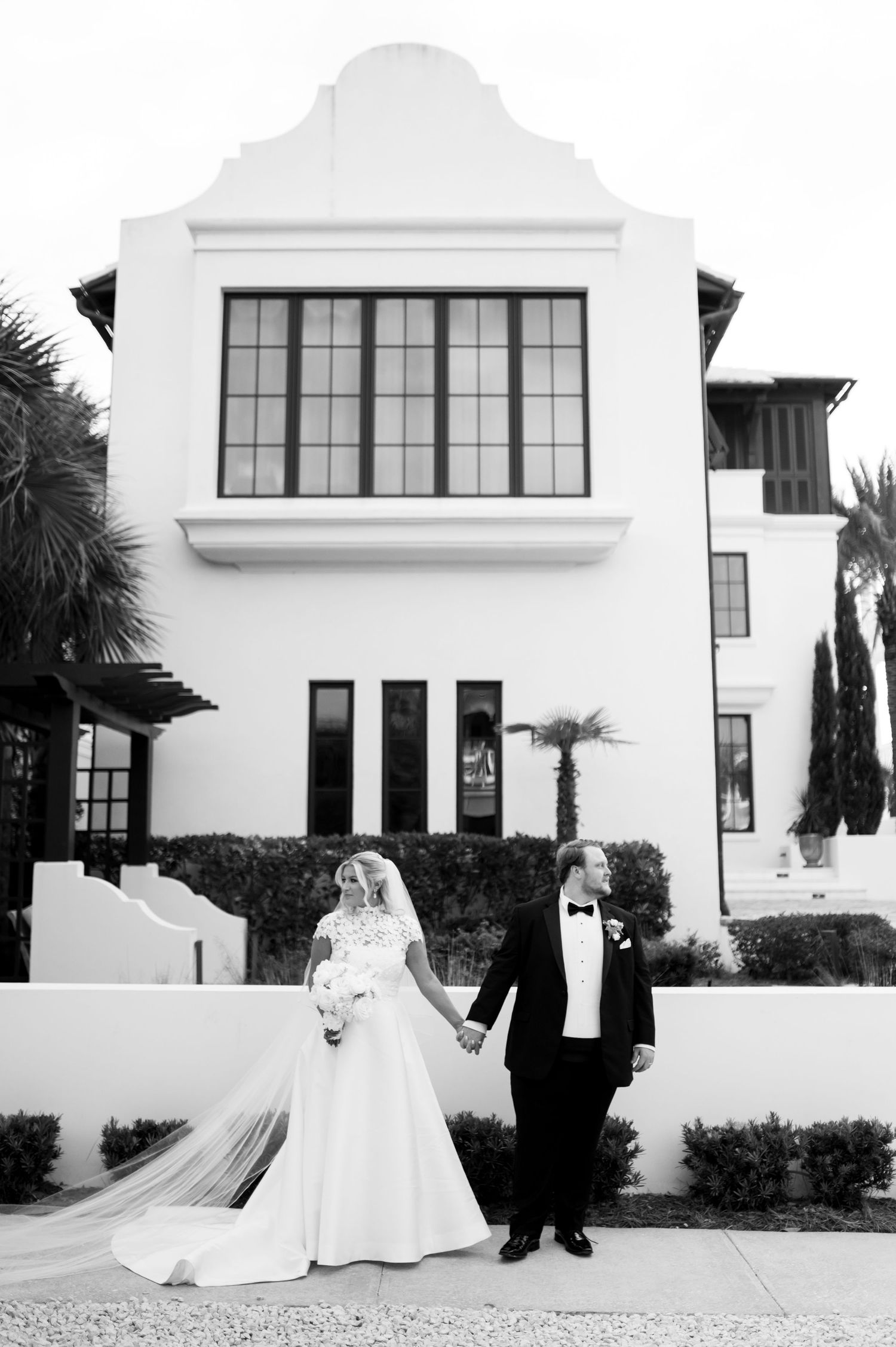 Elegant black and white wedding portraits taken outside a modern white building with palm trees.