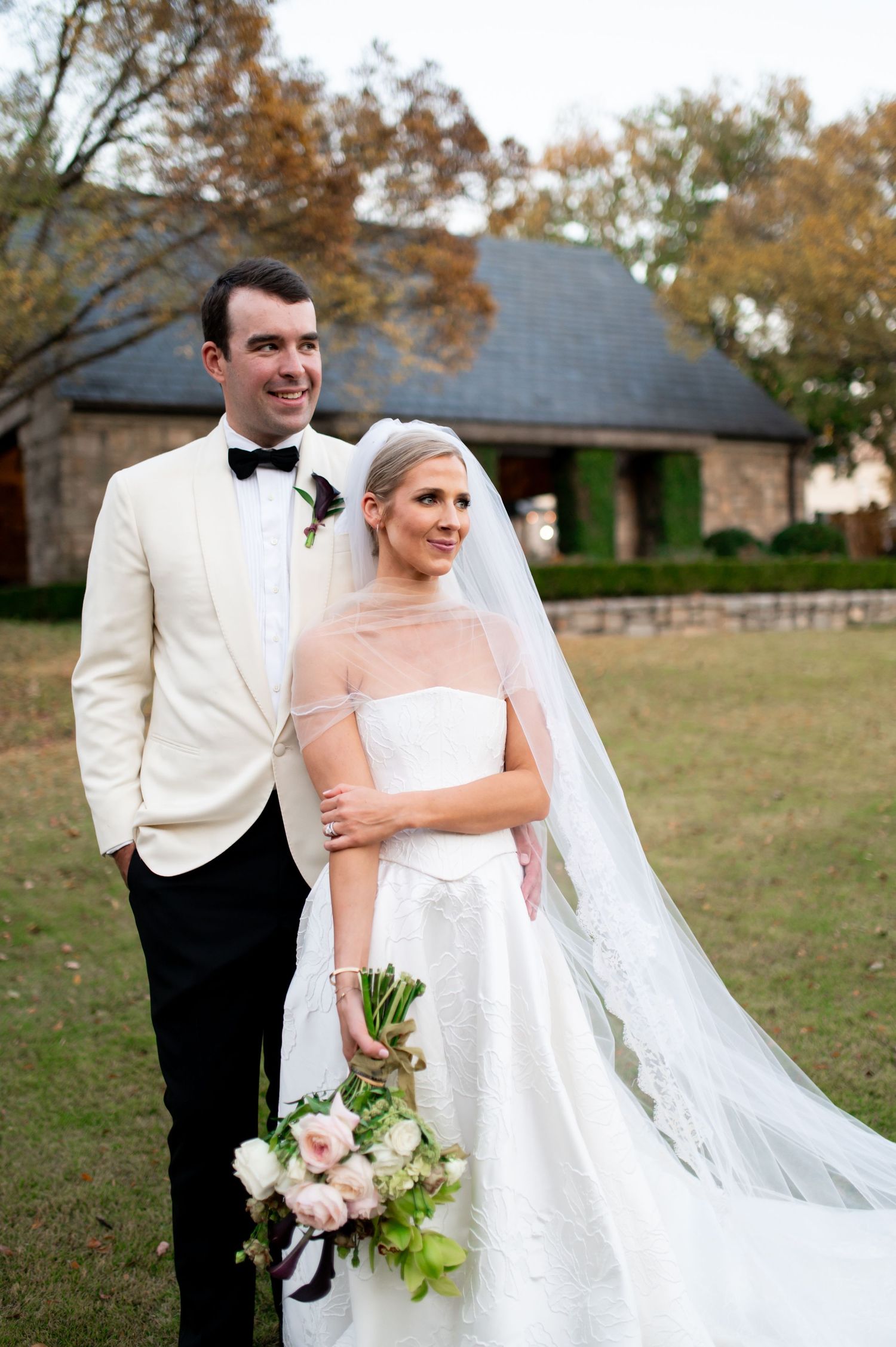 Wedding couple poses for portraits outdoors with the bride holding a pink and white bouquet.