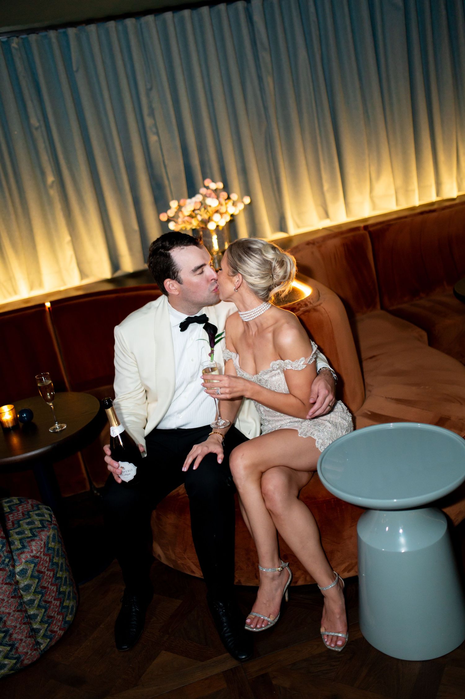 Couple shares intimate moment on leather couch during evening celebration.