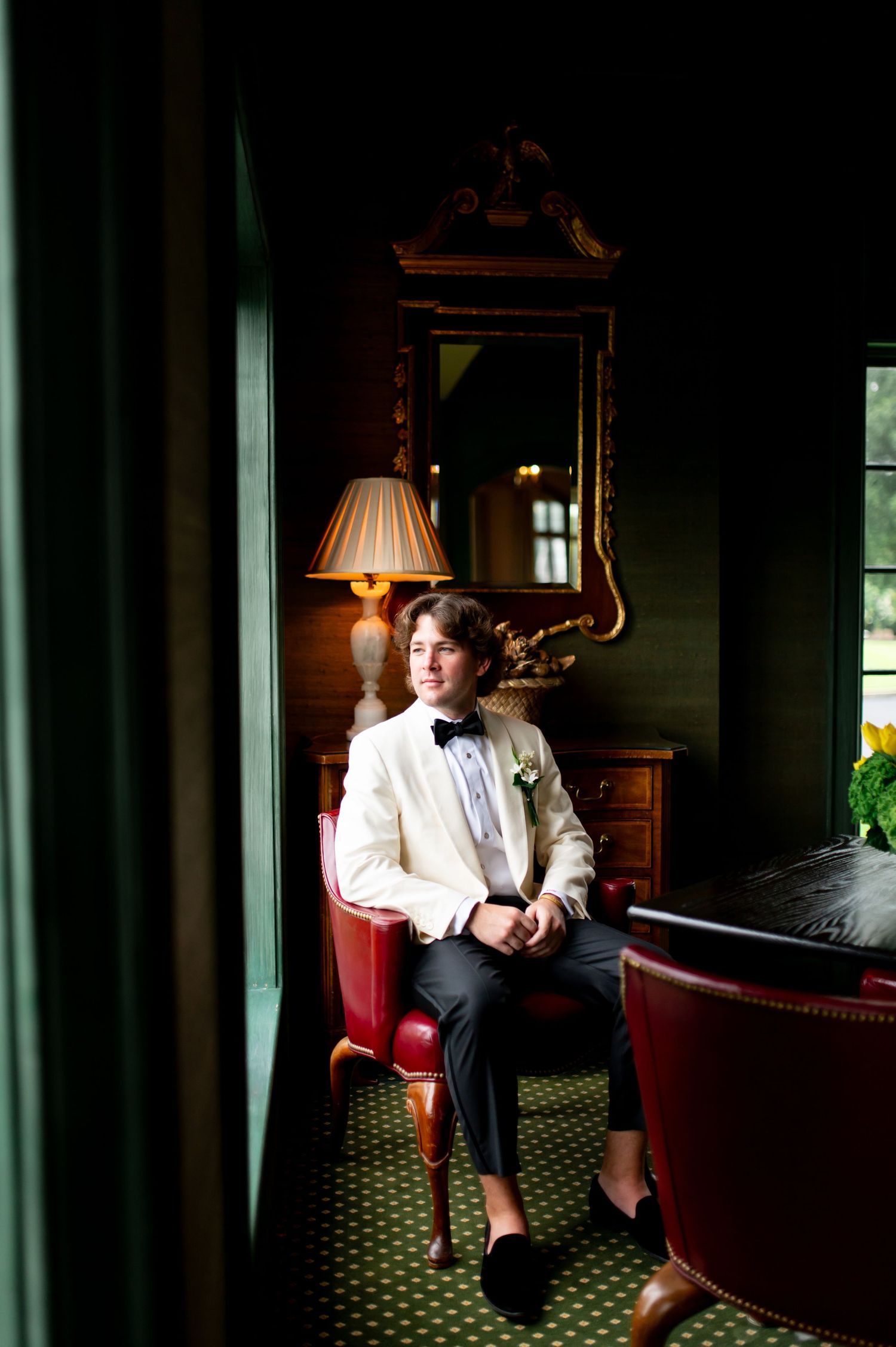 Moody portrait of someone relaxing in formal attire on red furniture in dark room.