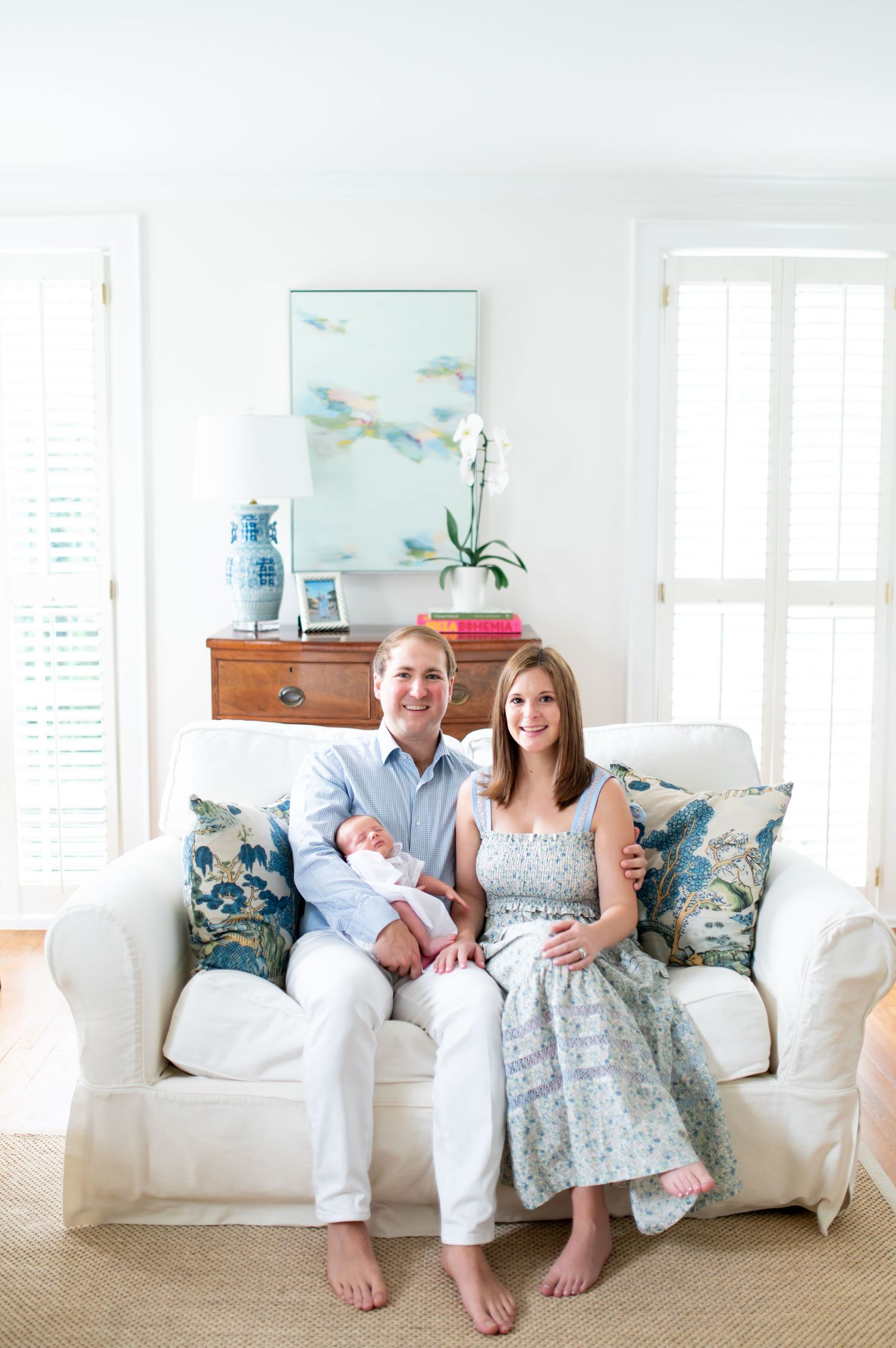A couple sits together on a white couch with decorative blue throw pillows in a bright, airy room.